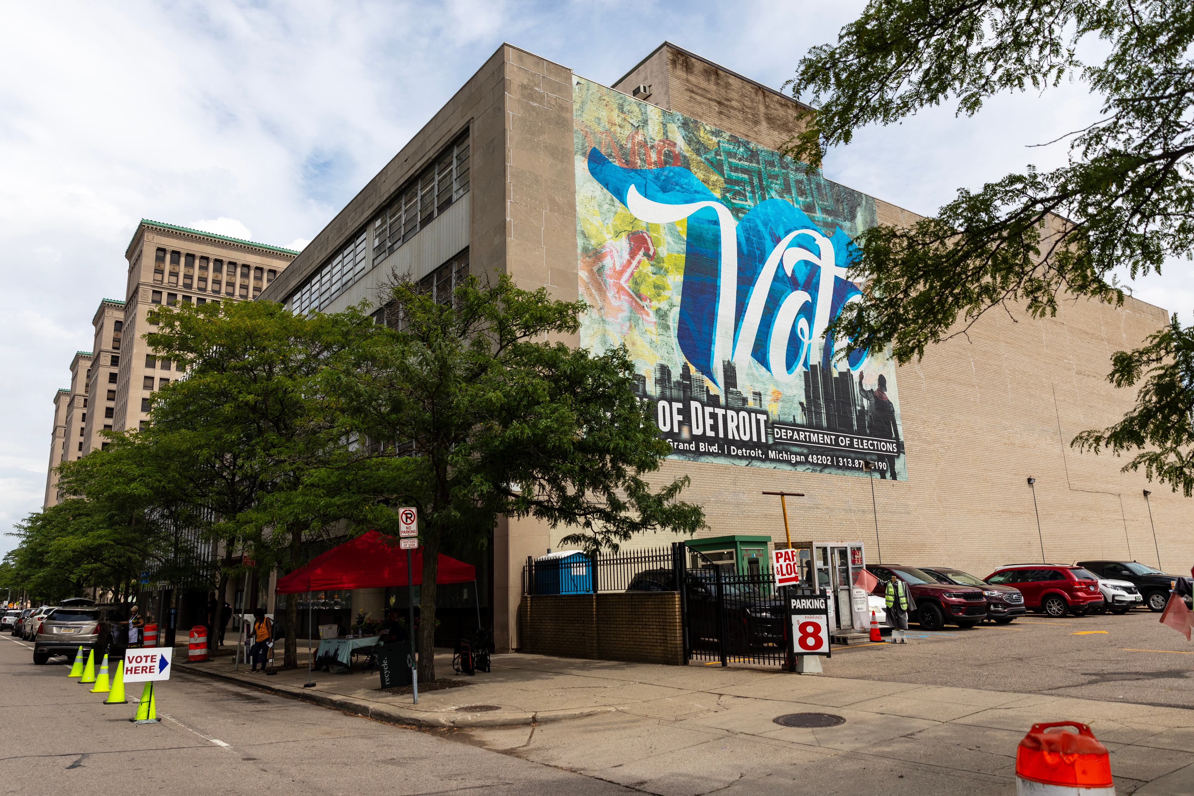 A large building with a mural on the side with green trees and cars along the street.
