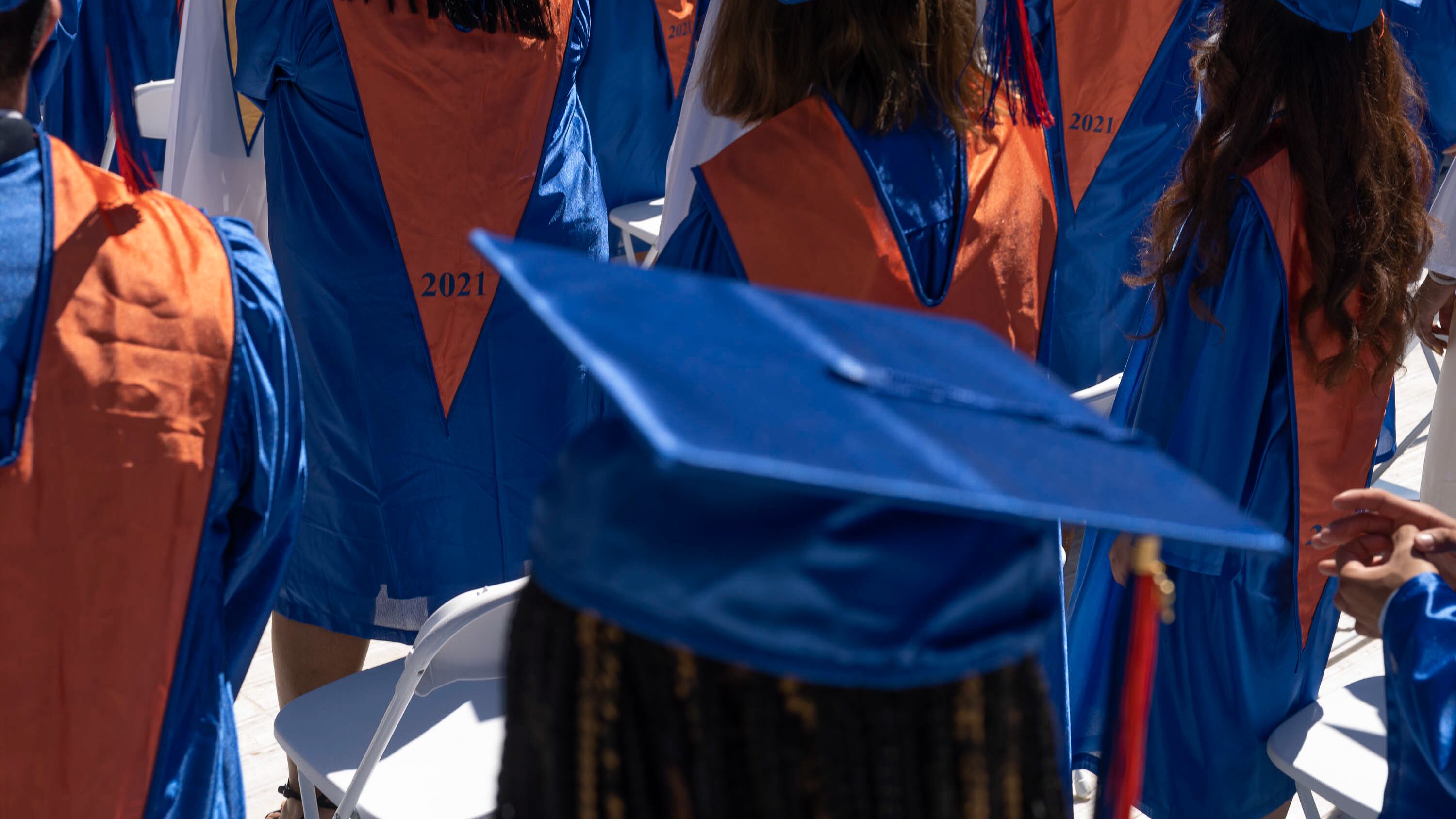 A close up of graduates wearing blue gowns and mortar boards with gold stoles.