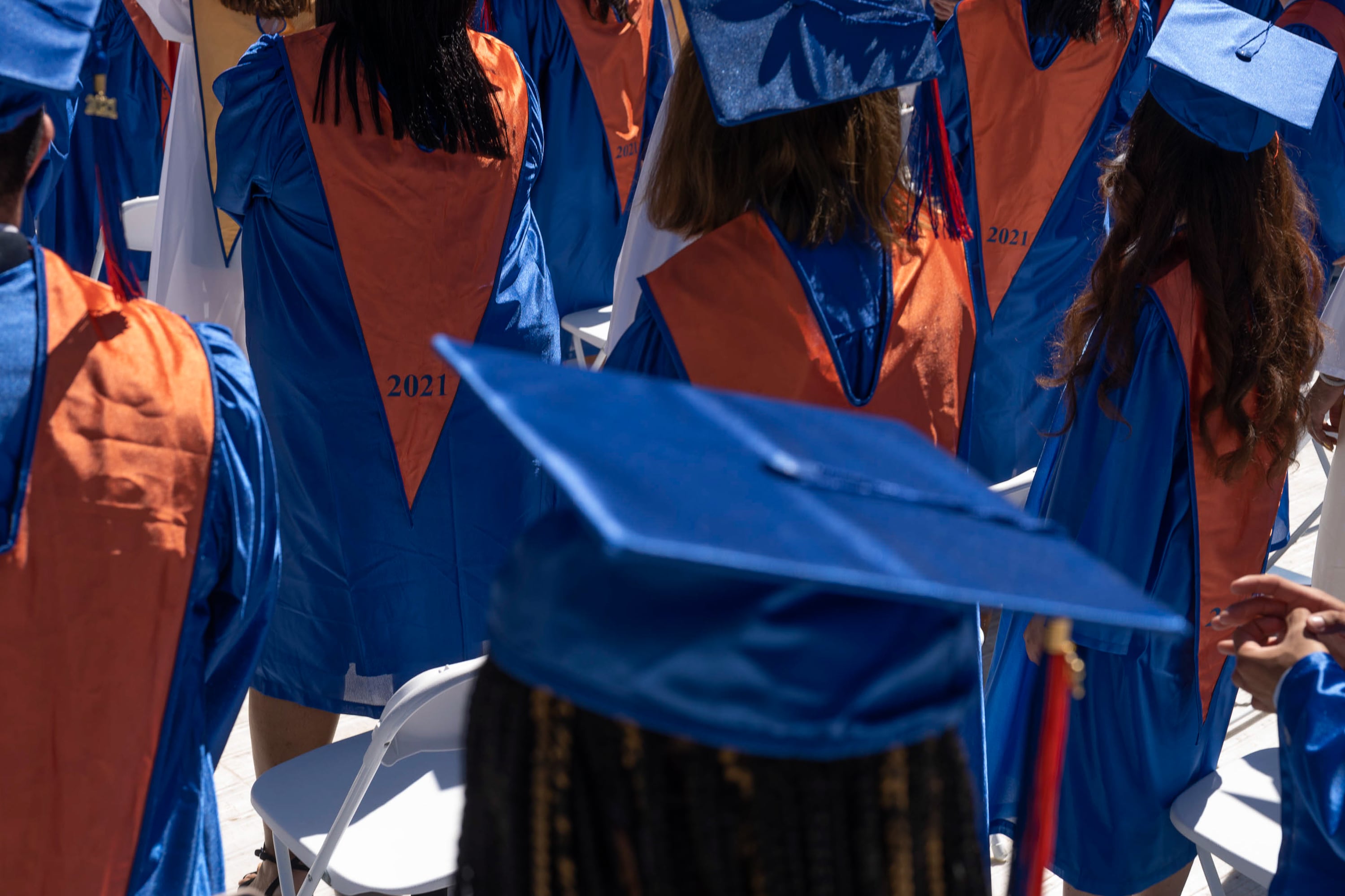 A close up of graduates wearing blue gowns and mortar boards with gold stoles.