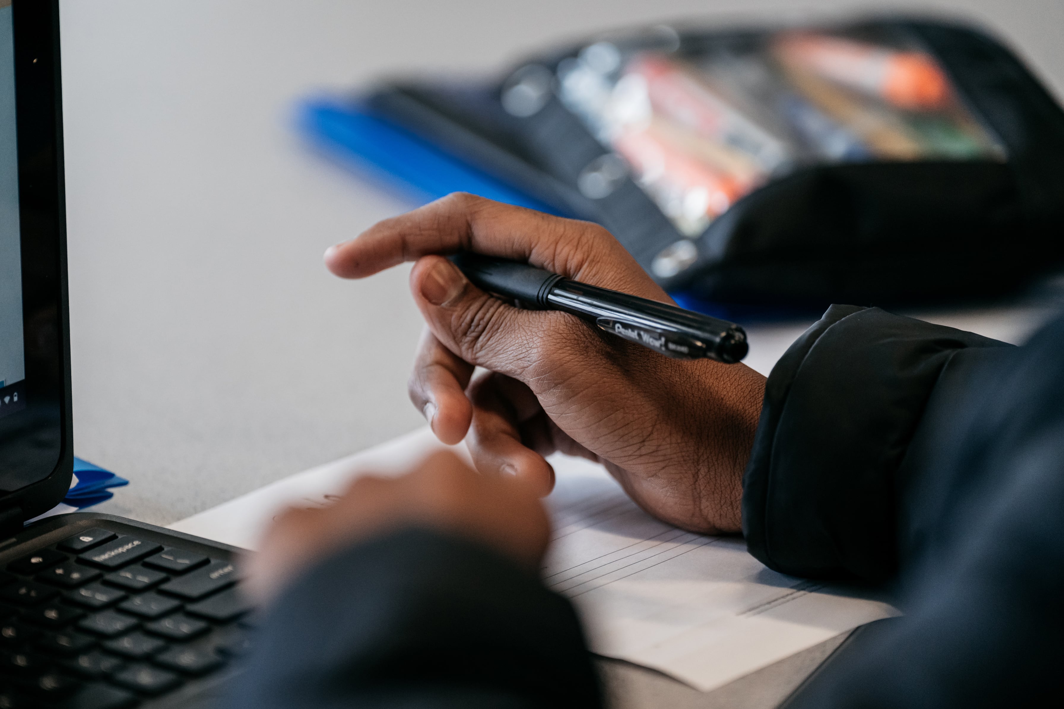 A hand is holding a pen in front of a computer screen.