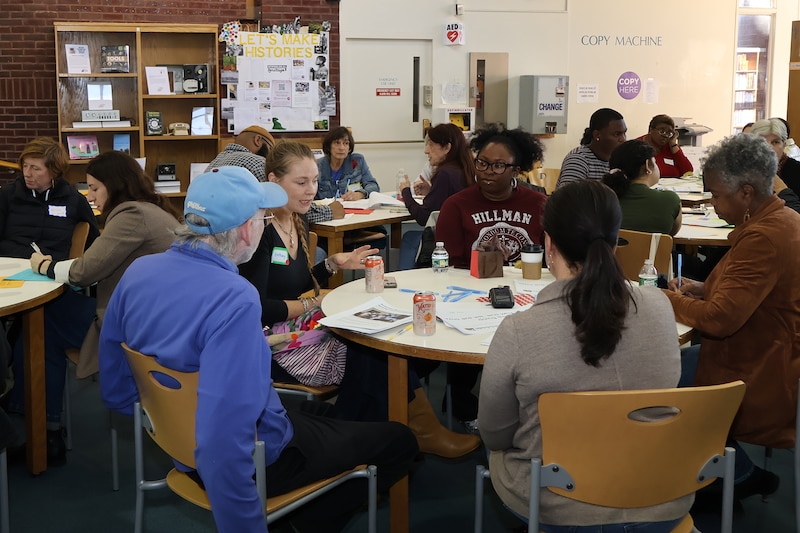 A photograph of a group of adults sitting in a school library.