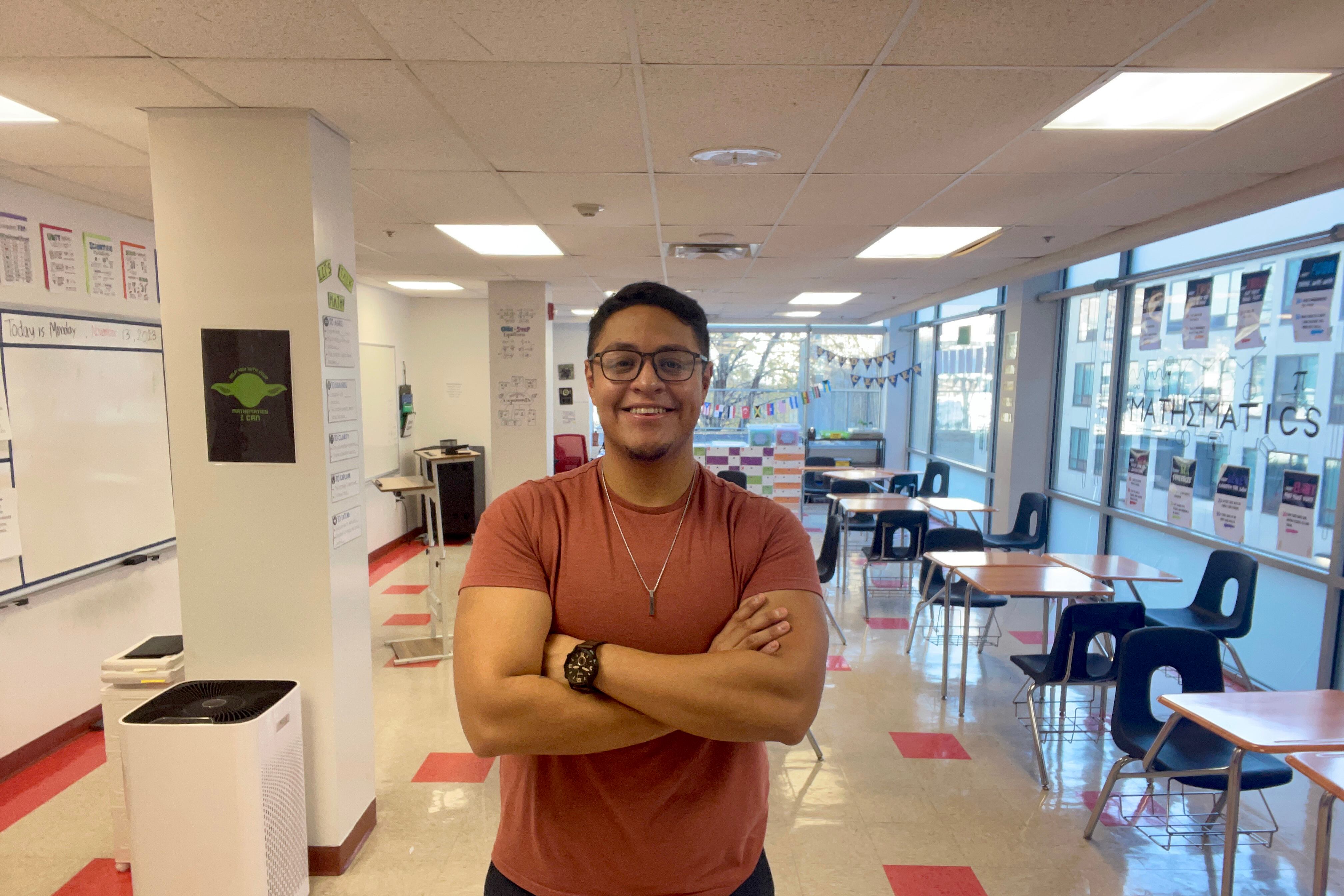 A man wearing an orange shirt folds his arms while standing in the middle of a large room and smiling at the camera.
