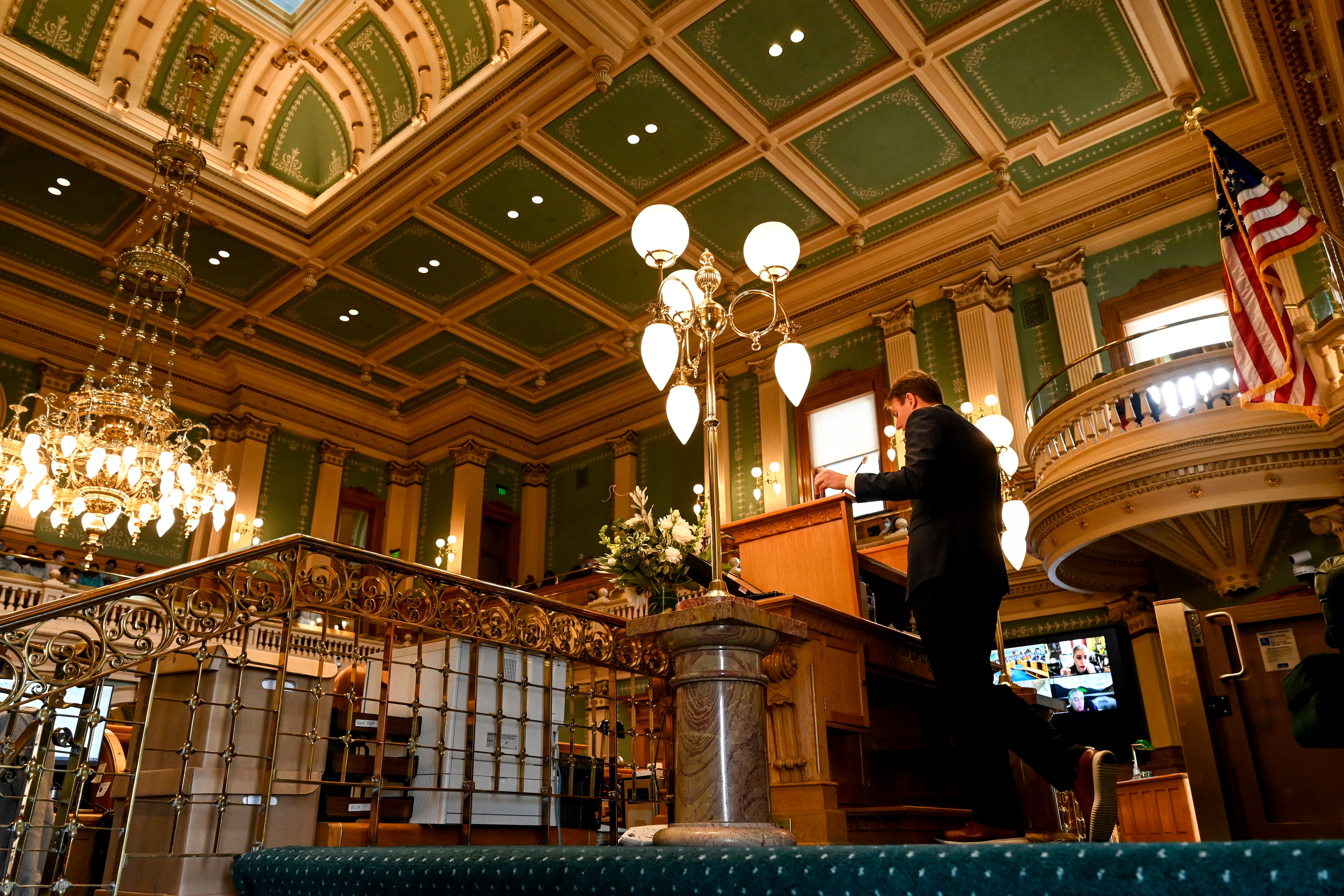 Colorado House Speaker Alec Garnett stands at the speaker’s podium with the view of the green, ornate ceiling of the House chamber in view.