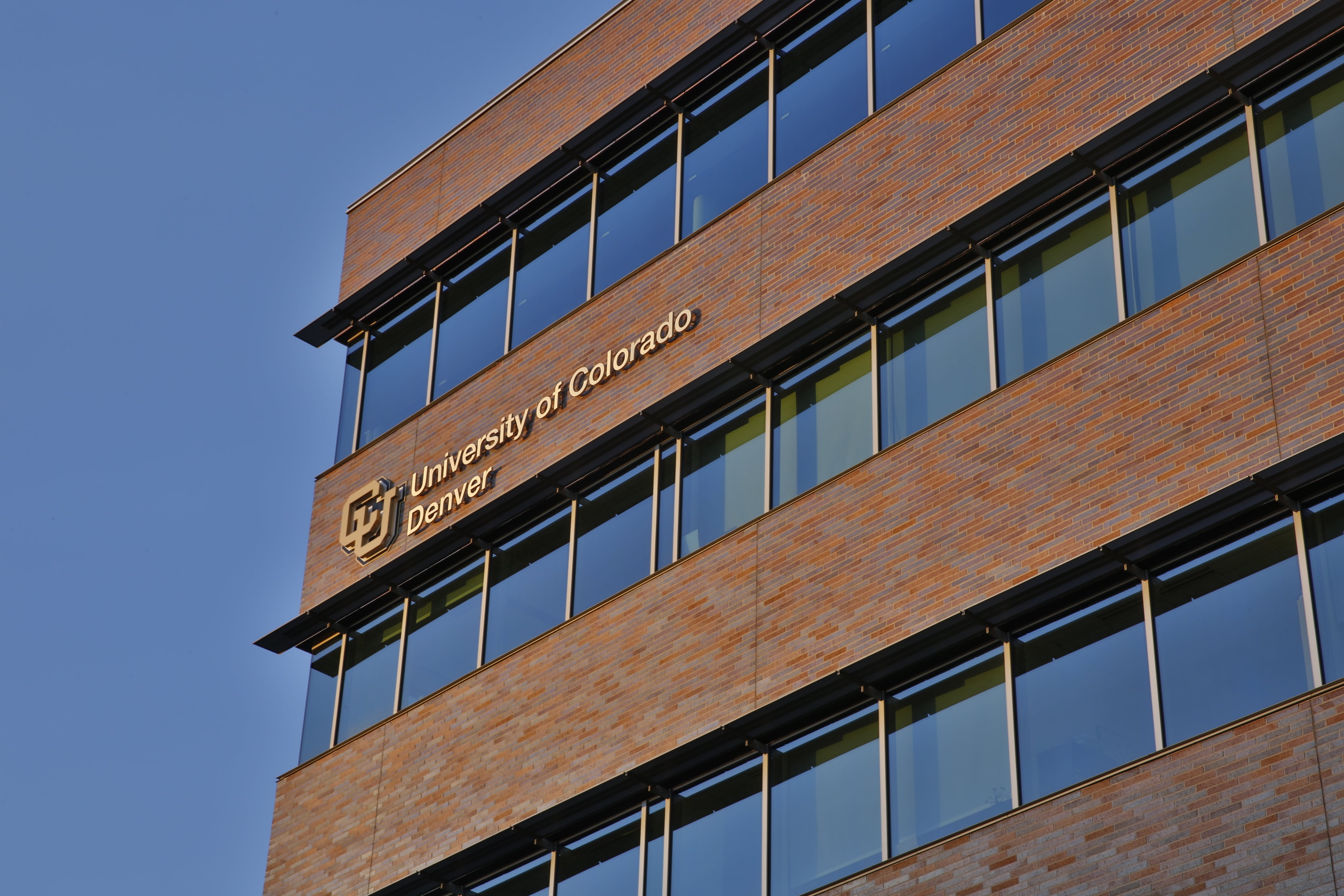 The brick and glass building of the University of Colorado Denver is seen against the blue sky.