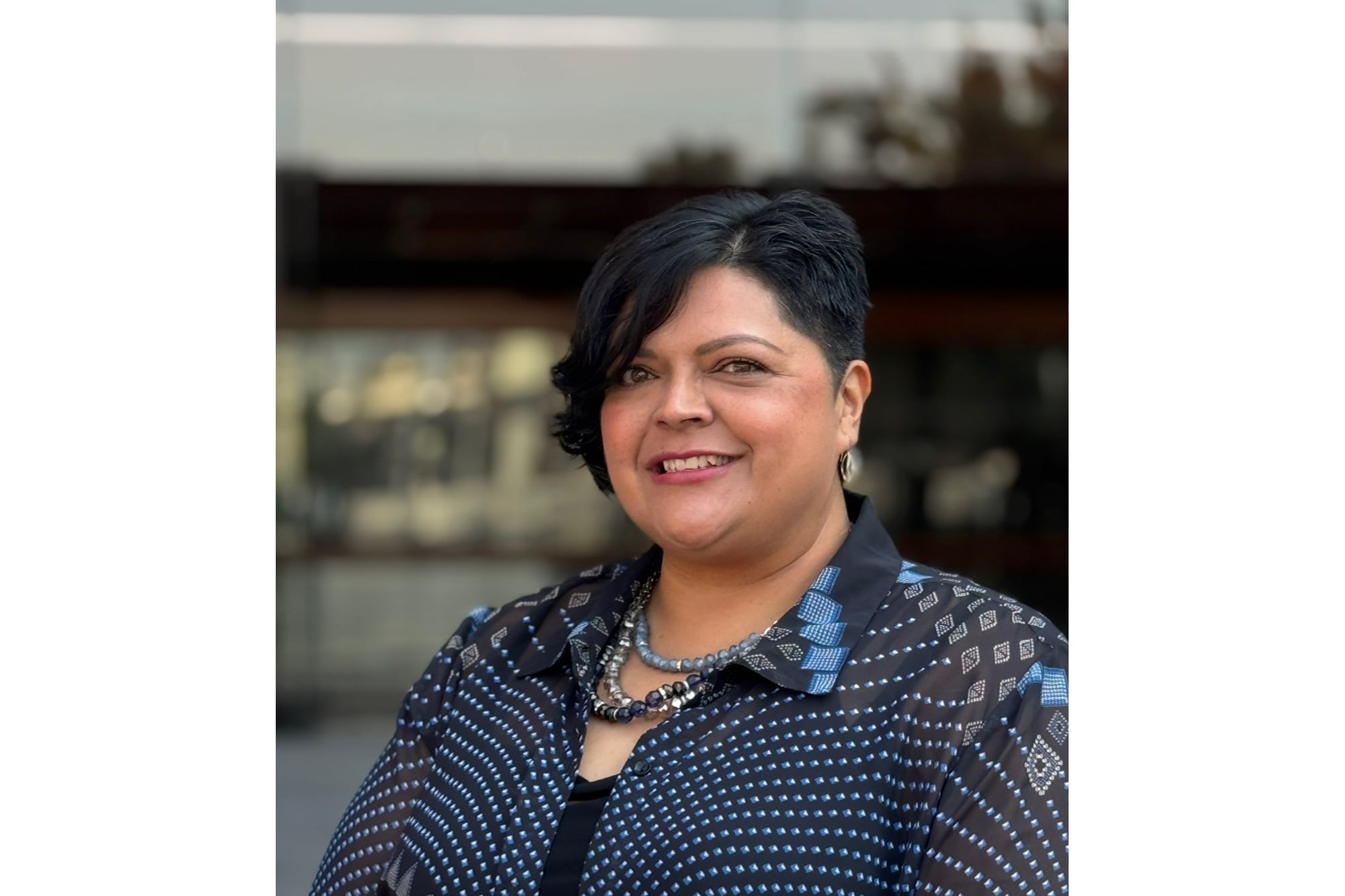 A photograph of a woman with dark, short hair and wearing a blouse poses for a portrait against a white background.