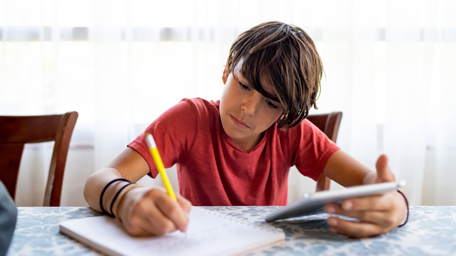 latinx preadolescent boy doing homework with a digital tablet at dining table