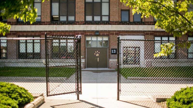 Detroit’s Southeastern High School, a large brick building surrounded by a chainlink fence. There is a logo of a yellow paw print on the door.