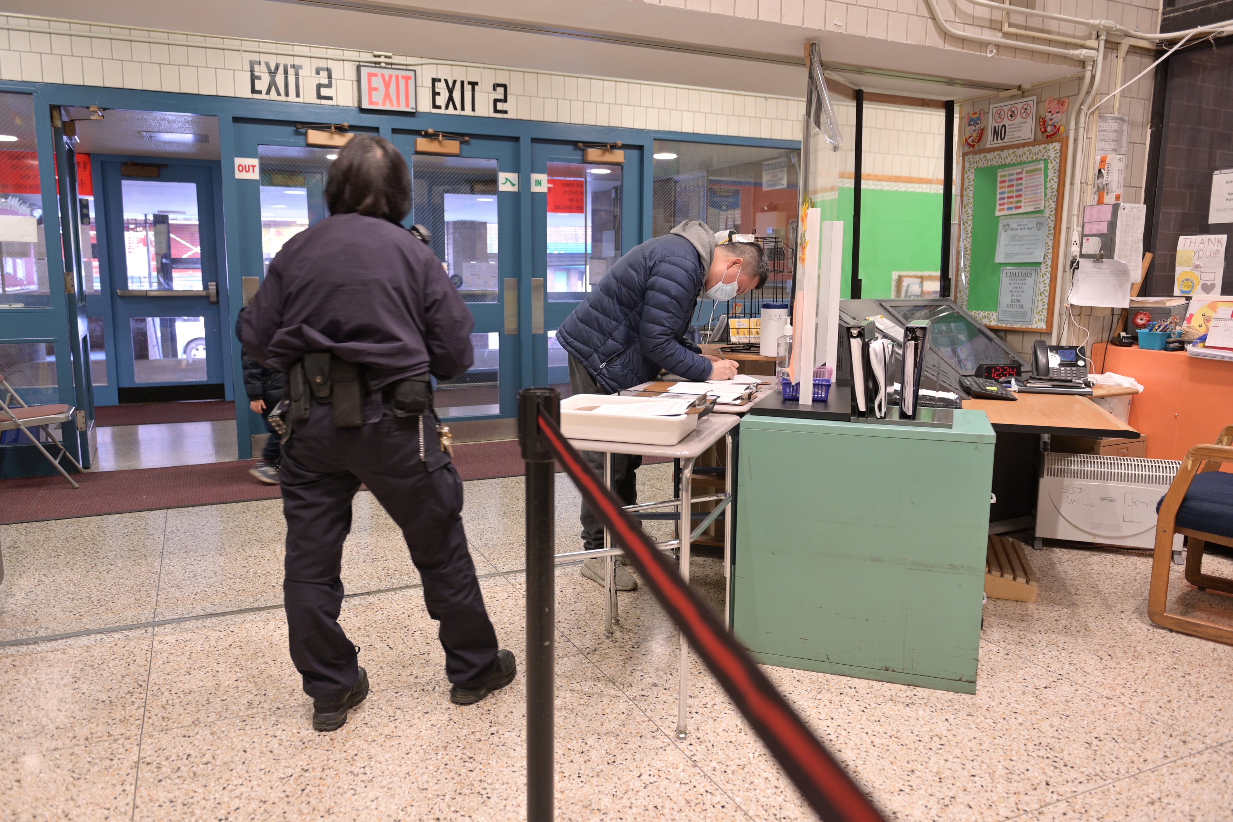 A school security guard watches a parent sign in at the entrance of their school.