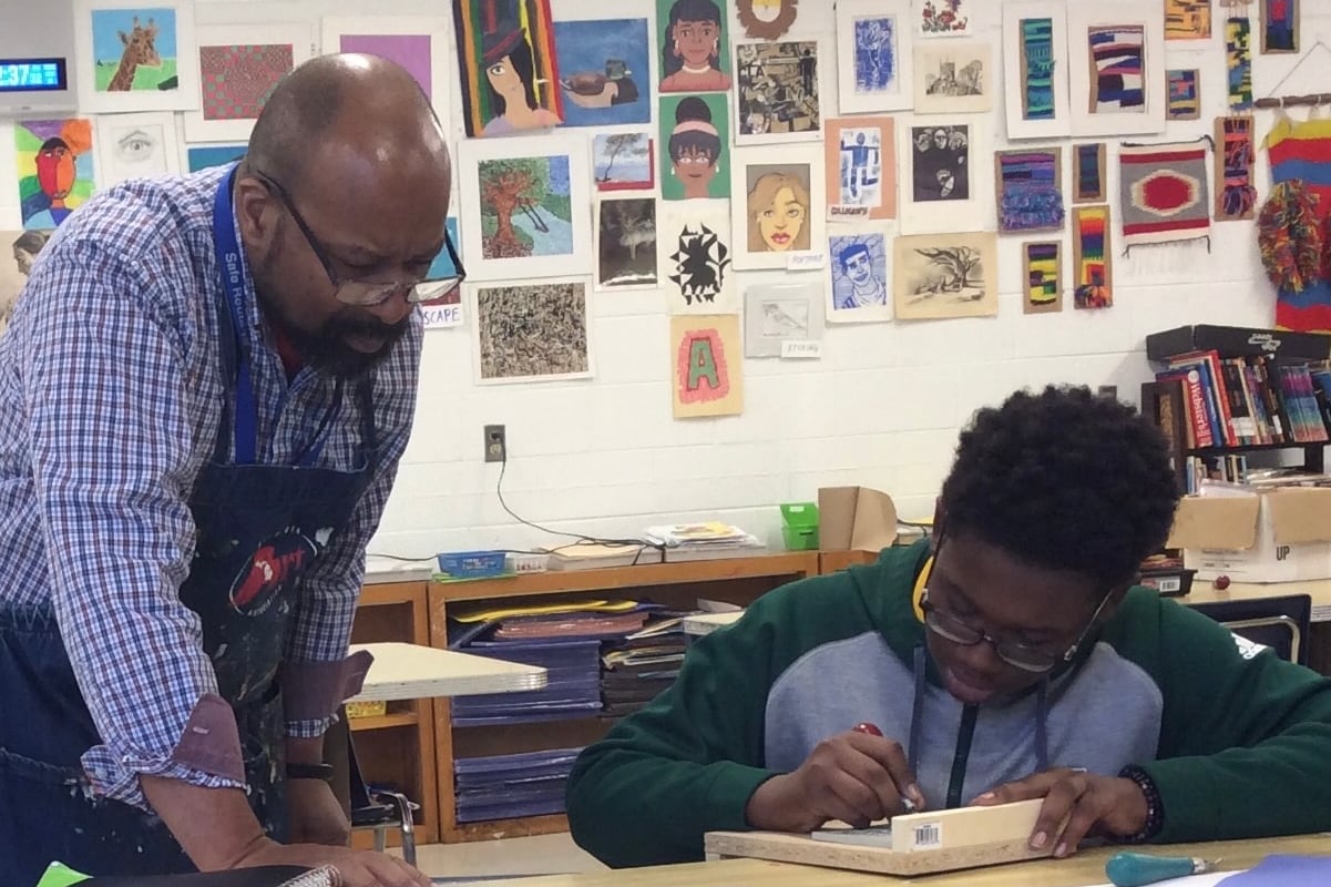 A teacher leans over to help a student during an art class.