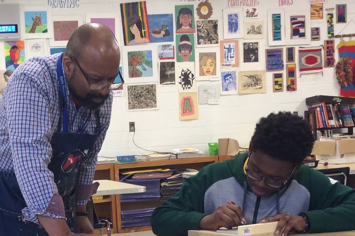 A teacher leans over to help a student during an art class.