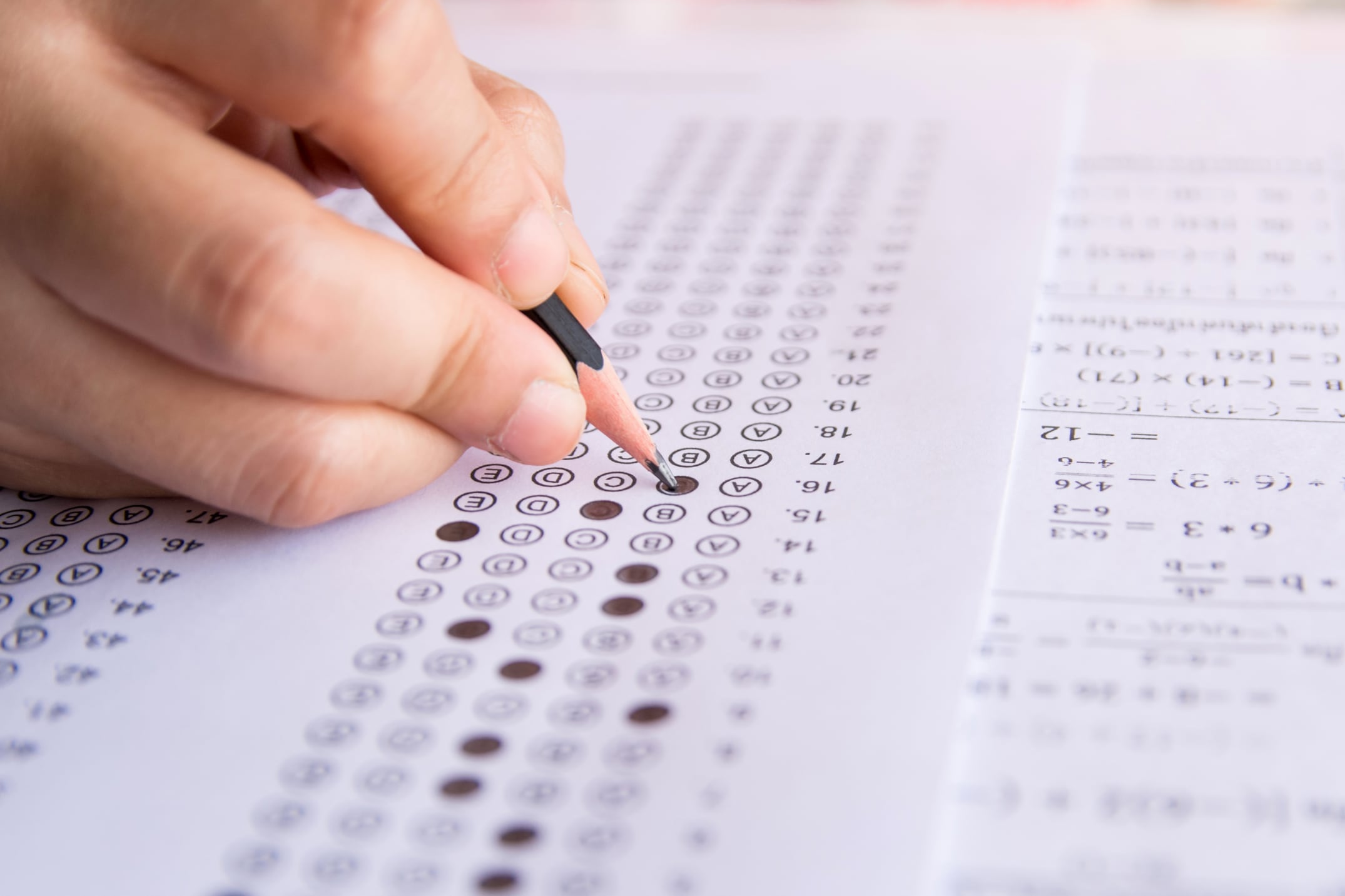 Students hand holding pencil writing selected choice on answer sheets and Mathematics question sheets. students testing doing examination. school exam