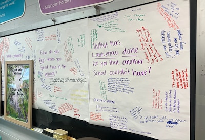 A photograph of a large hand written sign taped onto a dry erase board in a school classroom.