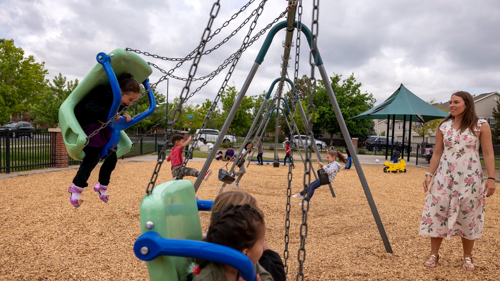 A teacher watches her students swing on a swing set on a school playground.