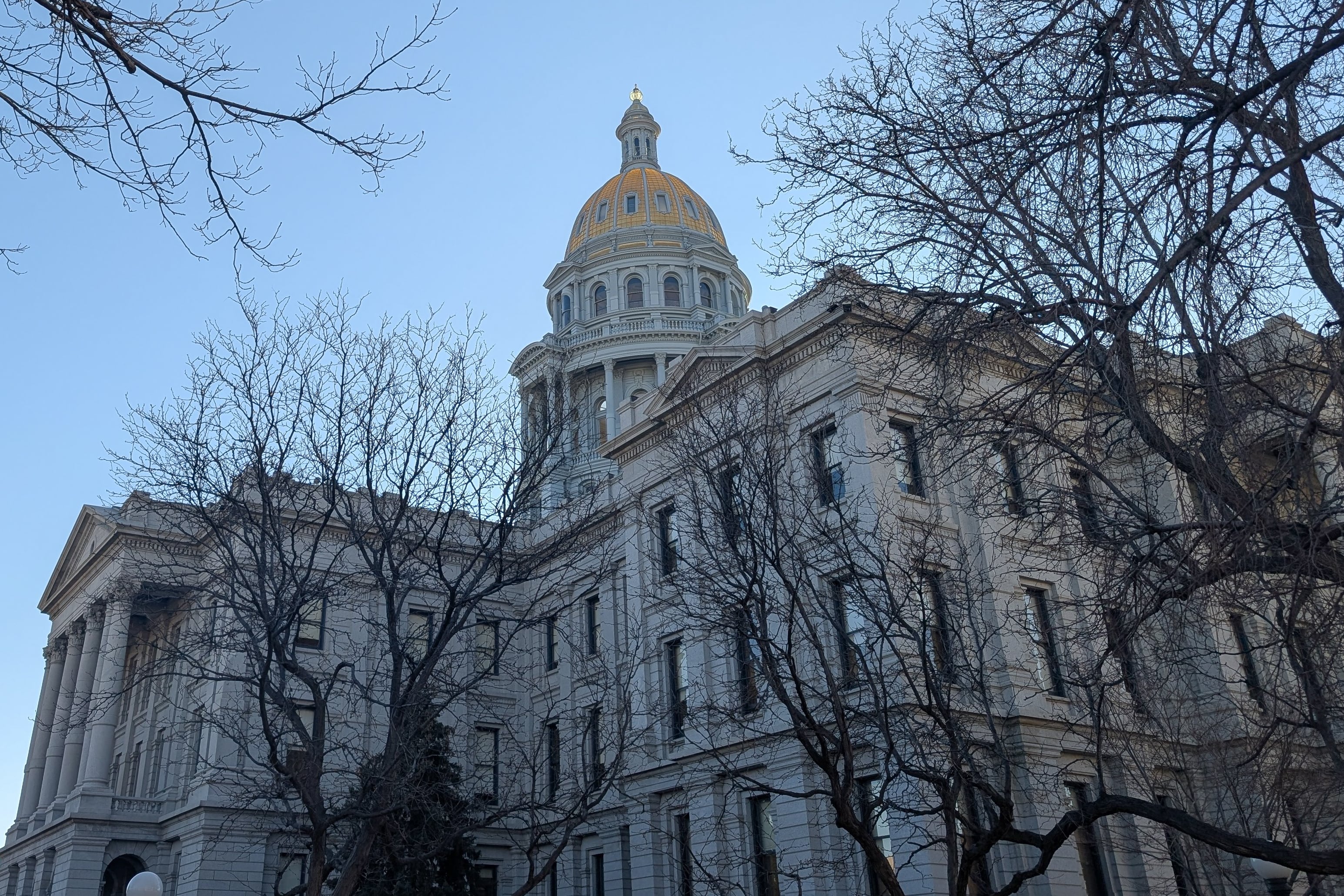 The grey Colorado Capitol with its gold dome against an evening blue sky.