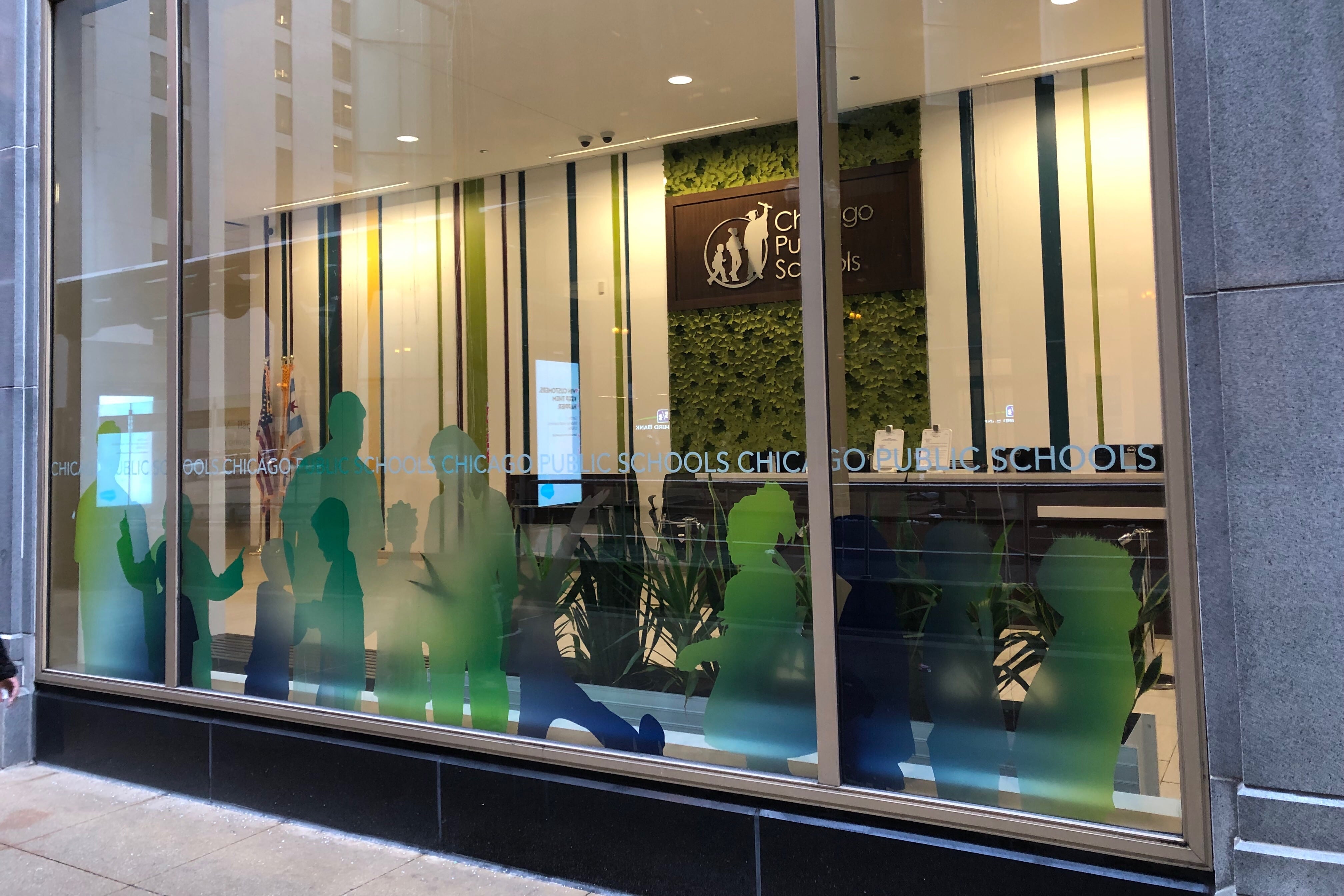 The facade of Chicago Public Schools headquarters, with the district’s sign hanging on the wall behind windows with green silhouettes of students.