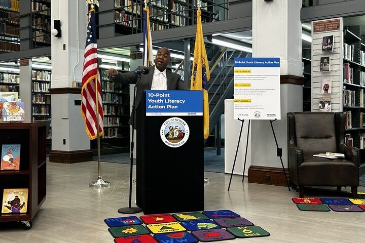 A man wearing a suit stands behind the podium in the Newark Public Library.