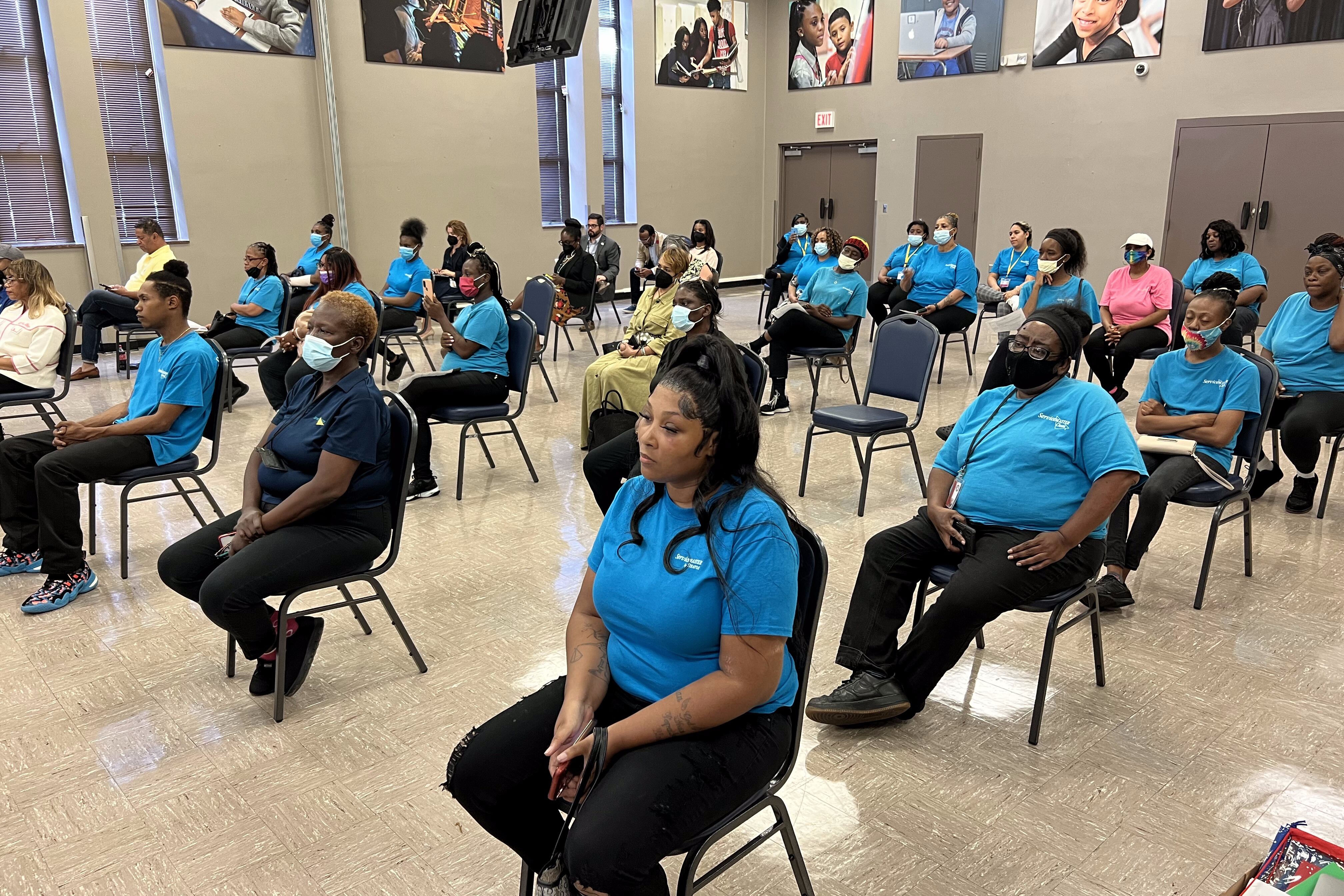 People wearing teal “ServiceMaster Clean” tshirts sit in the Memphis-Shelby County Schools Board of Education auditorium.