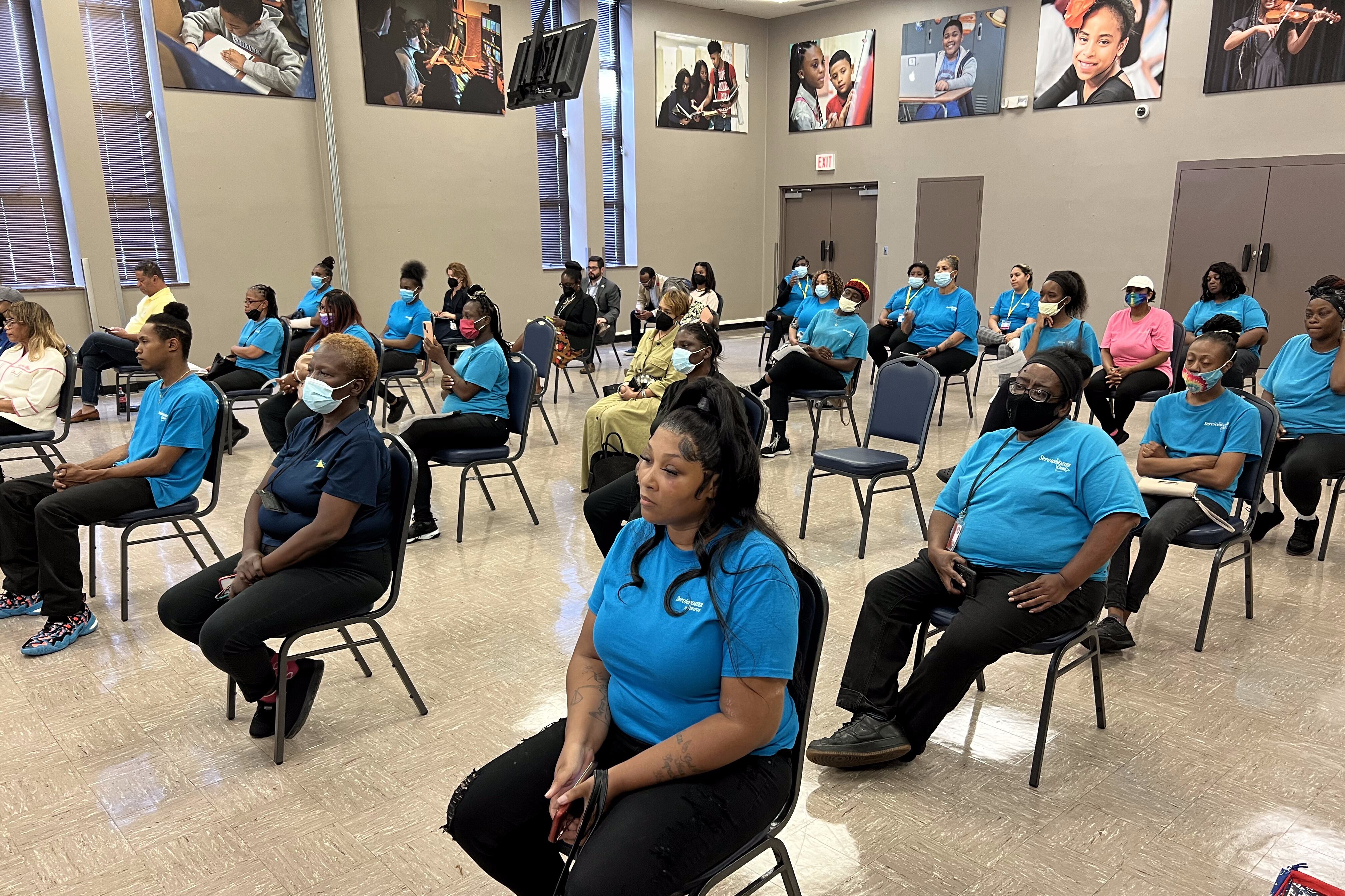 People wearing teal “ServiceMaster Clean” tshirts sit in the Memphis-Shelby County Schools Board of Education auditorium.