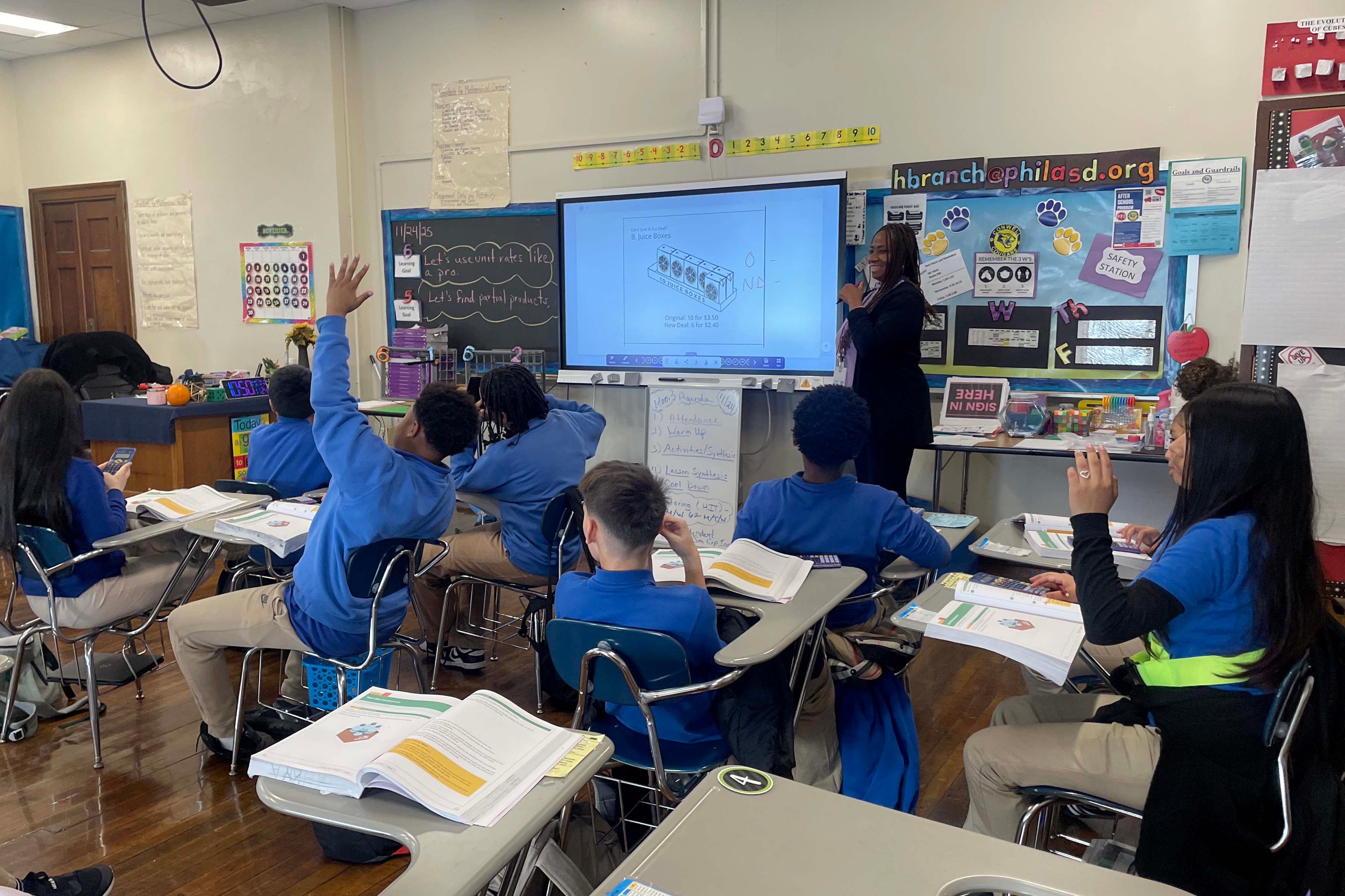 A photograph of middle school students all wearing blue t-shirts sit at their desks in a classroom.