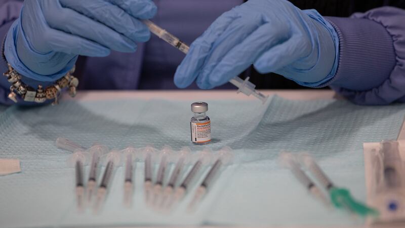 A close-up photo of a person’s hands wearing blue latex gloves, preparing a syringe for a COVID-19 vaccination.