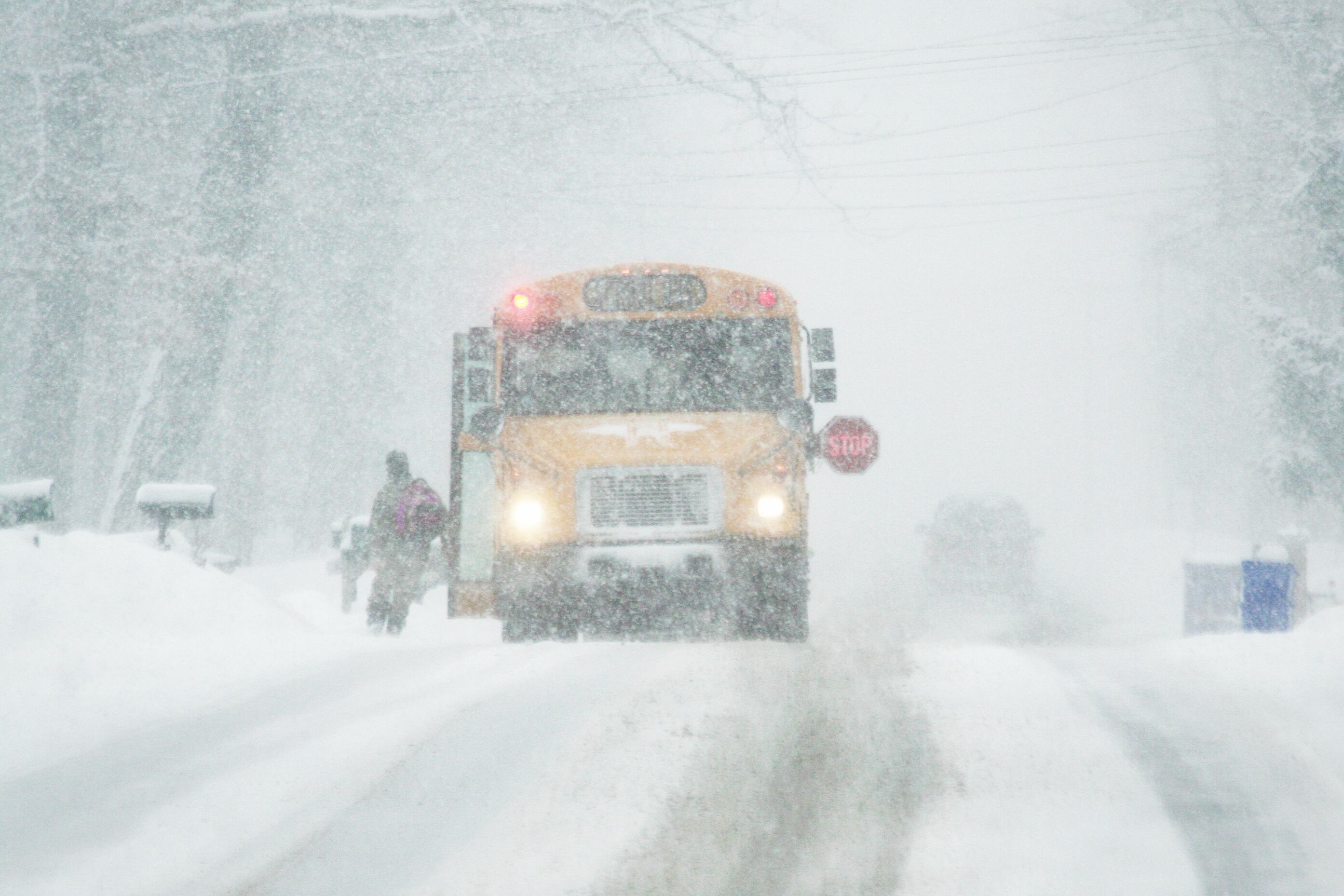 A yellow school bus travels on a snowy road during heavy snow flurries.