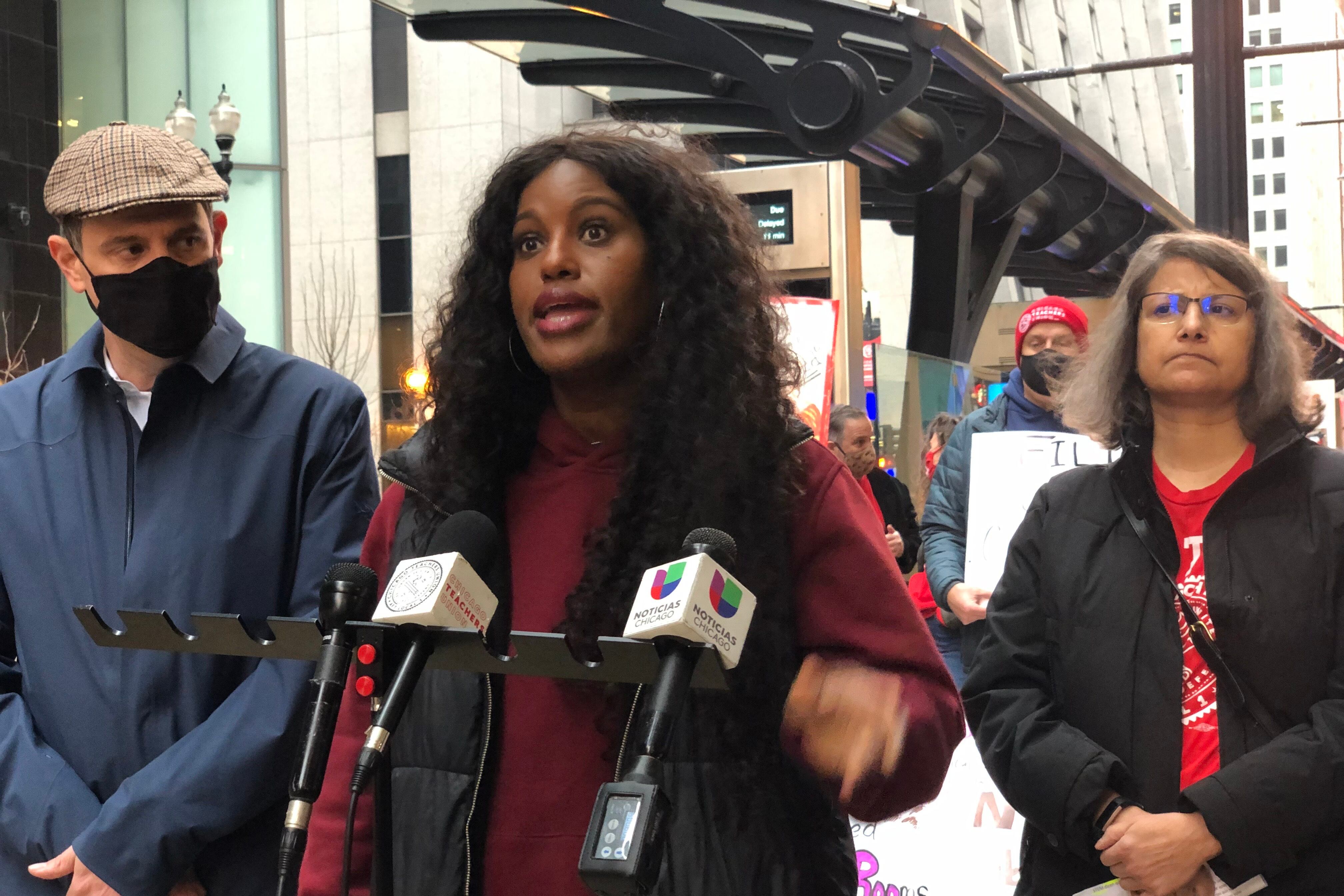A woman speaks at a podium flanked by a man in a face mask and another woman.