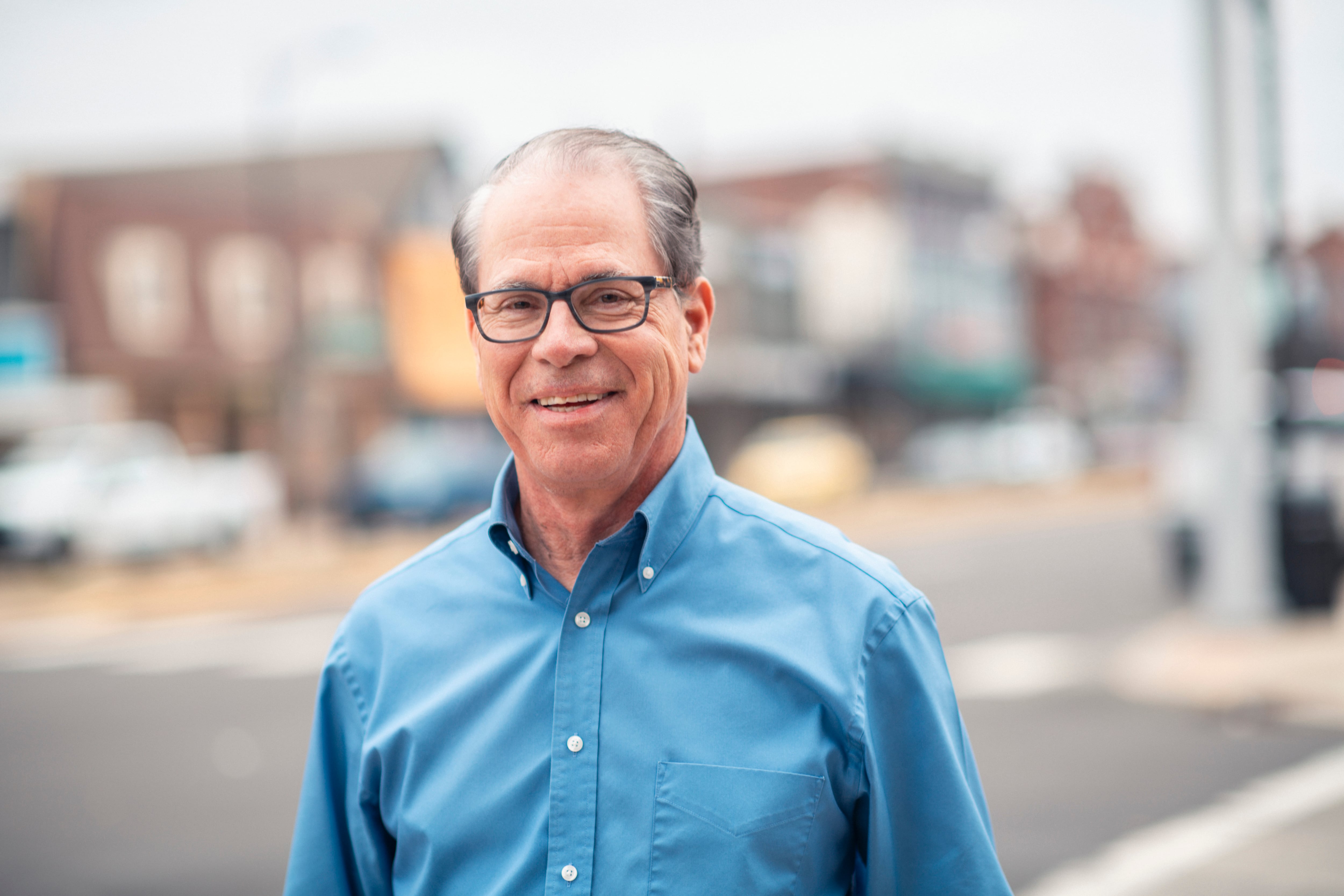 A man in a blue button up shirt stands outside.