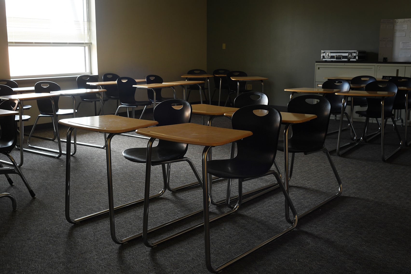 An empty classroom full of school desks with a large window in the background.