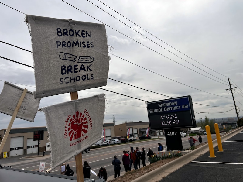 A group of adults stand outside some are holding signs or banners or a megaphone.