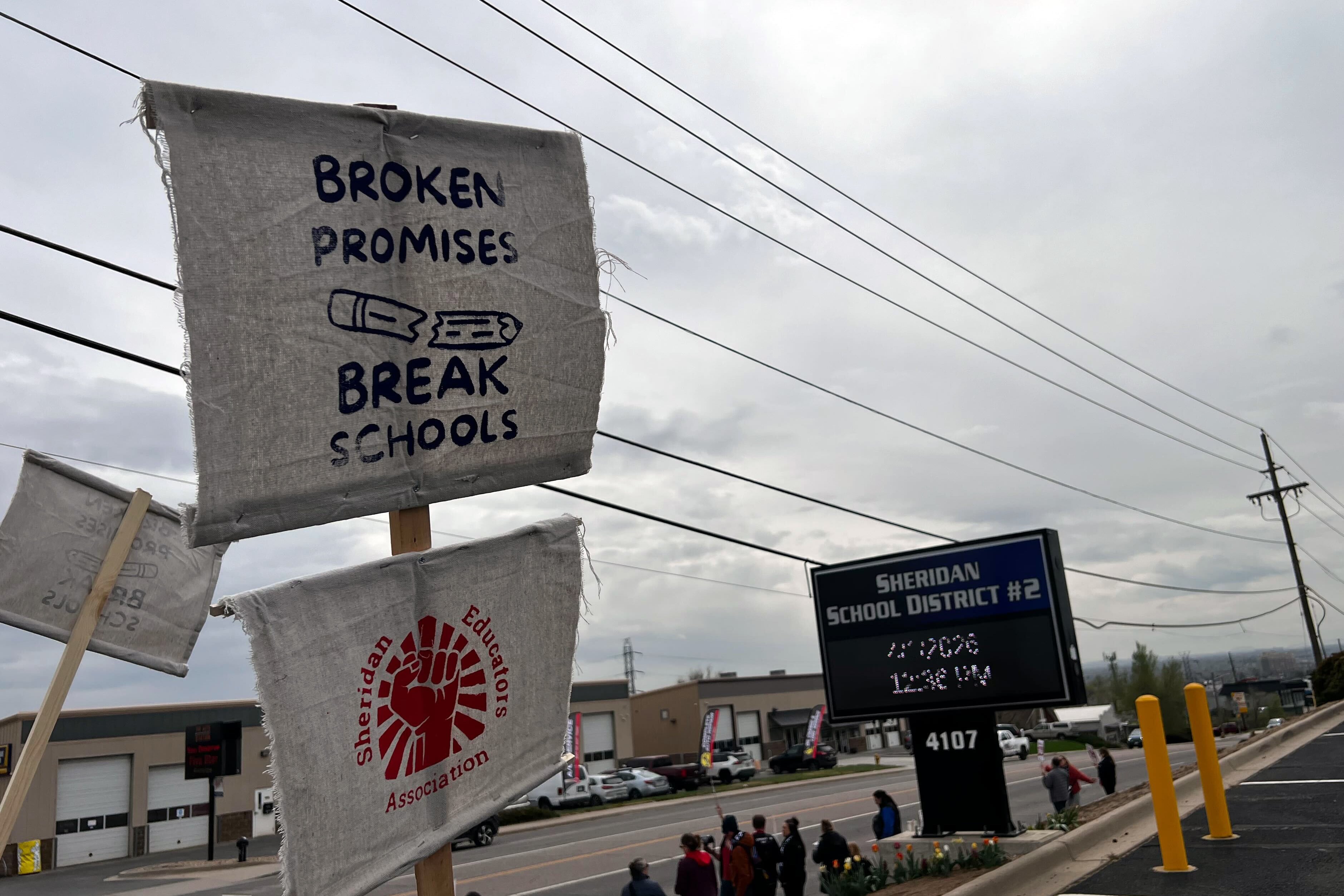 A group of adults stand outside some are holding signs or banners or a megaphone.