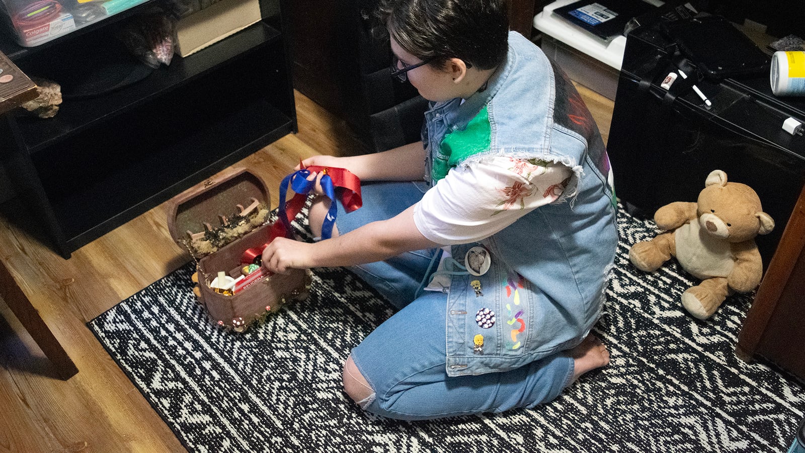A youth in jeans and a jeans vest sits on a floor