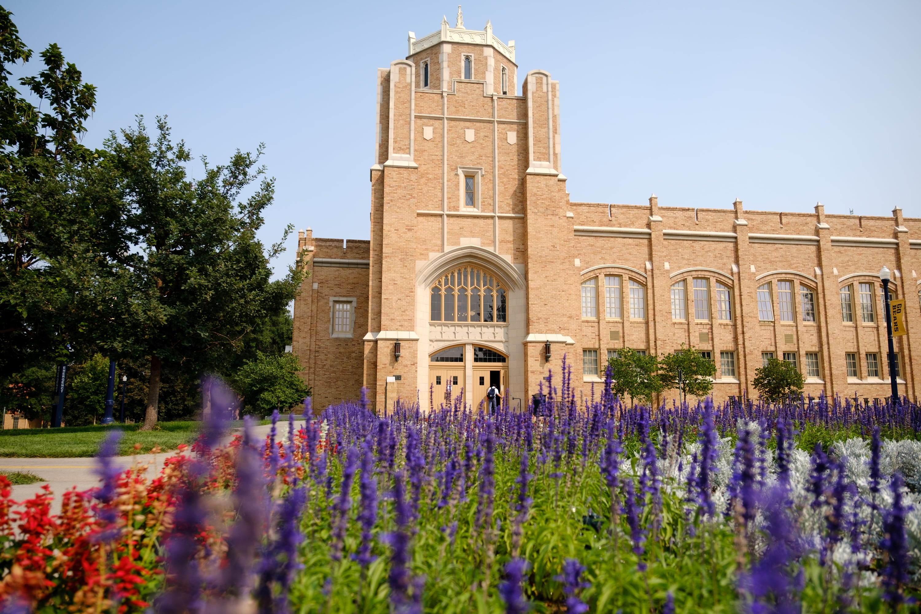 A large tan stone building sits behind a wall of colorful flowers.