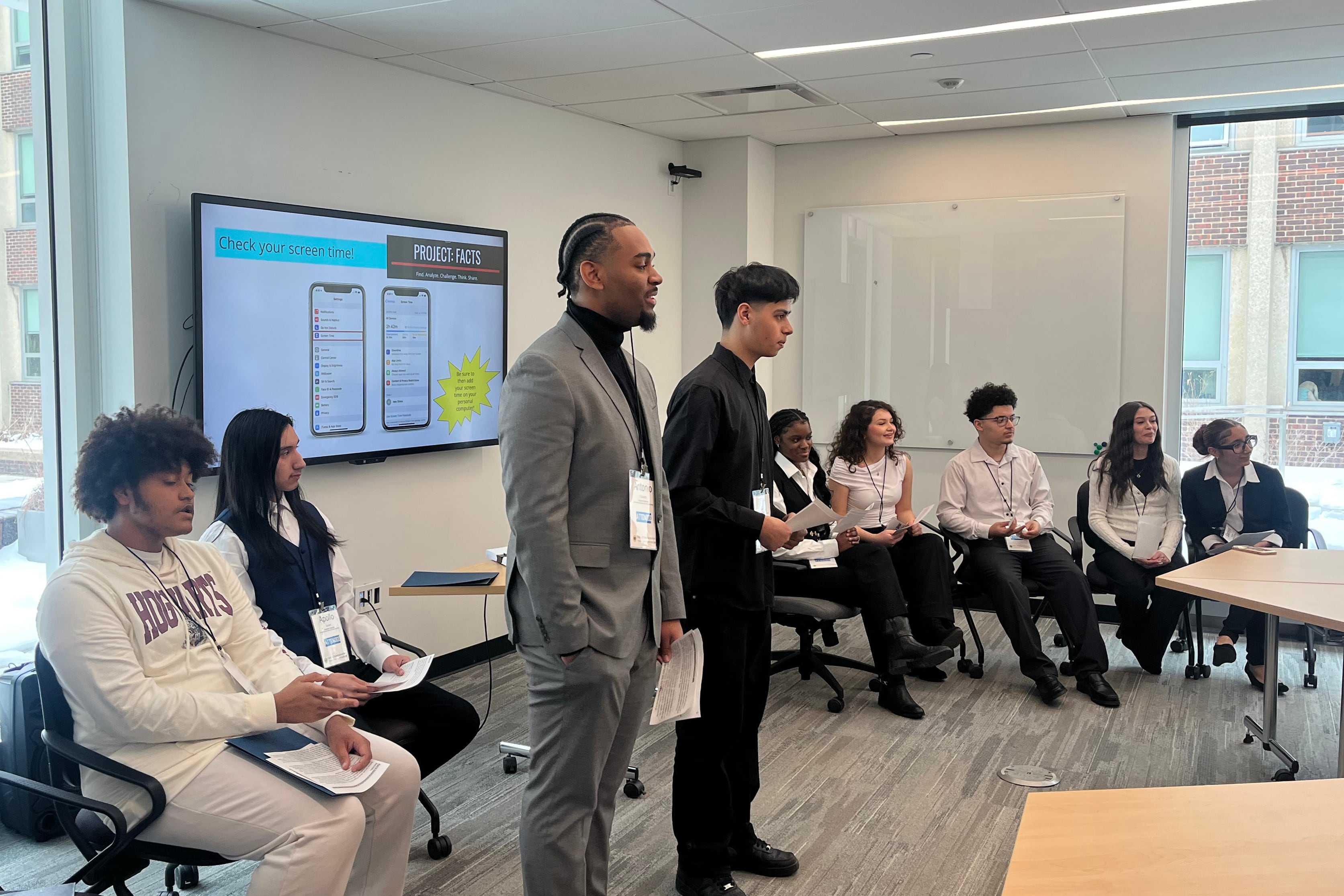 A photograph of a group of high school students all dressed up and presenting in a conference room.