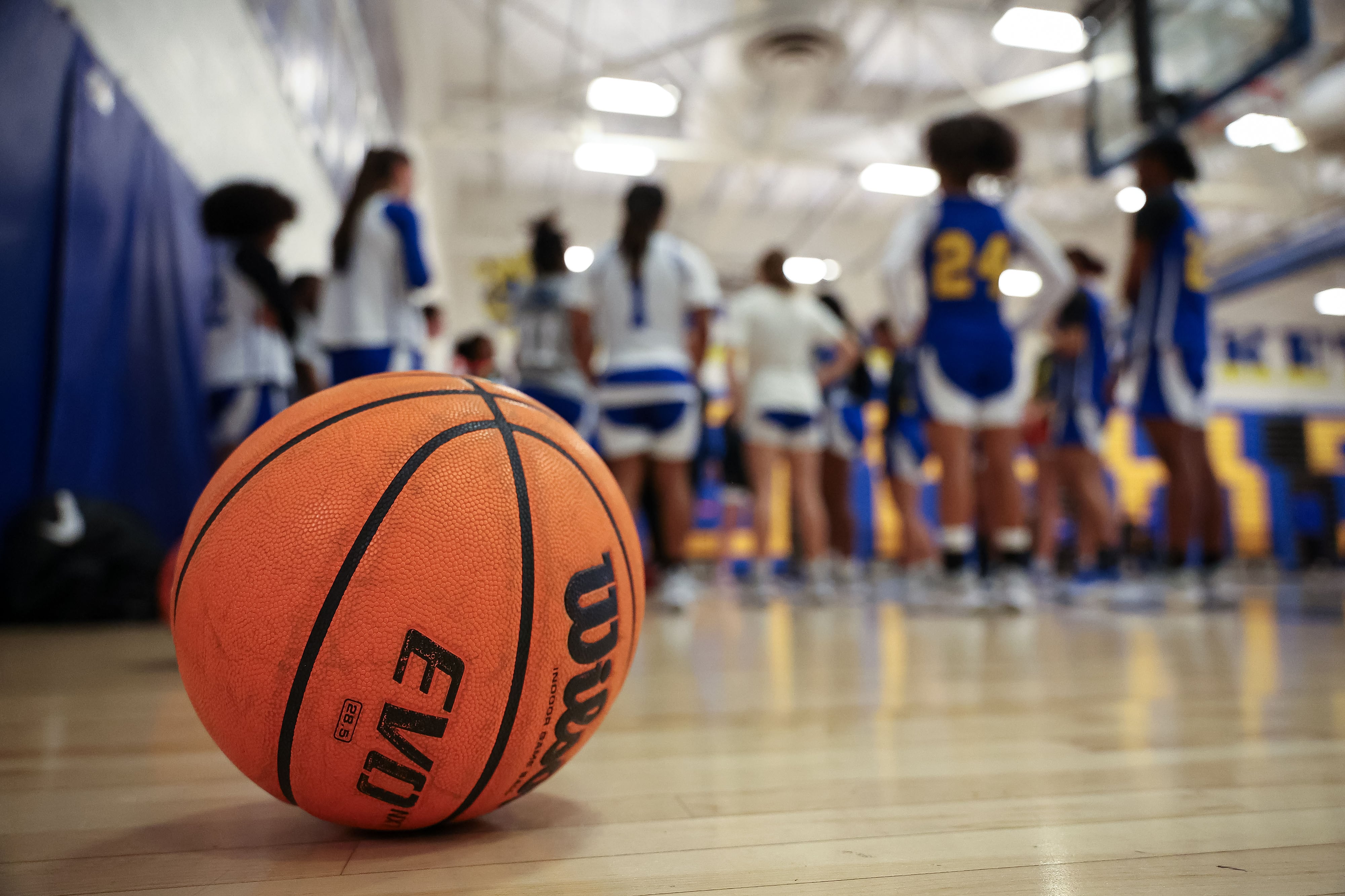 A high school basketball on the floor of a high school gym with a girl's basketball team in the background that is blurry.