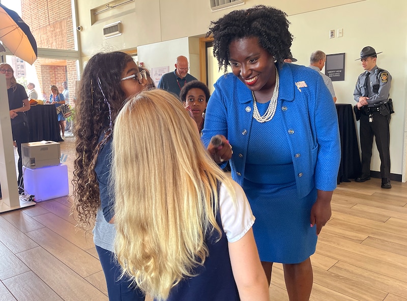 A woman in a blue suitdress speaks to two girls with long hair.