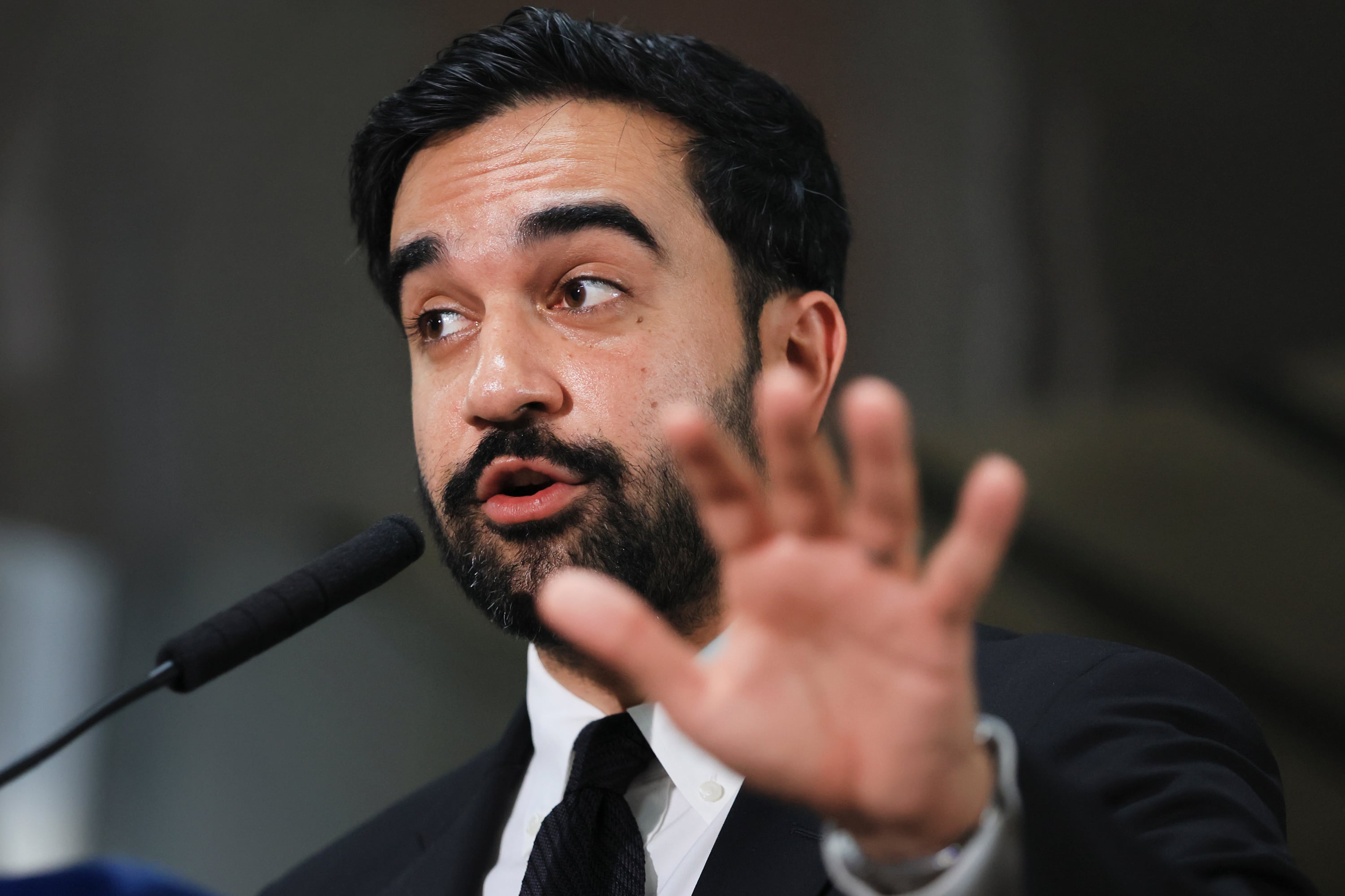 A male in a suit speaking into a microphone.