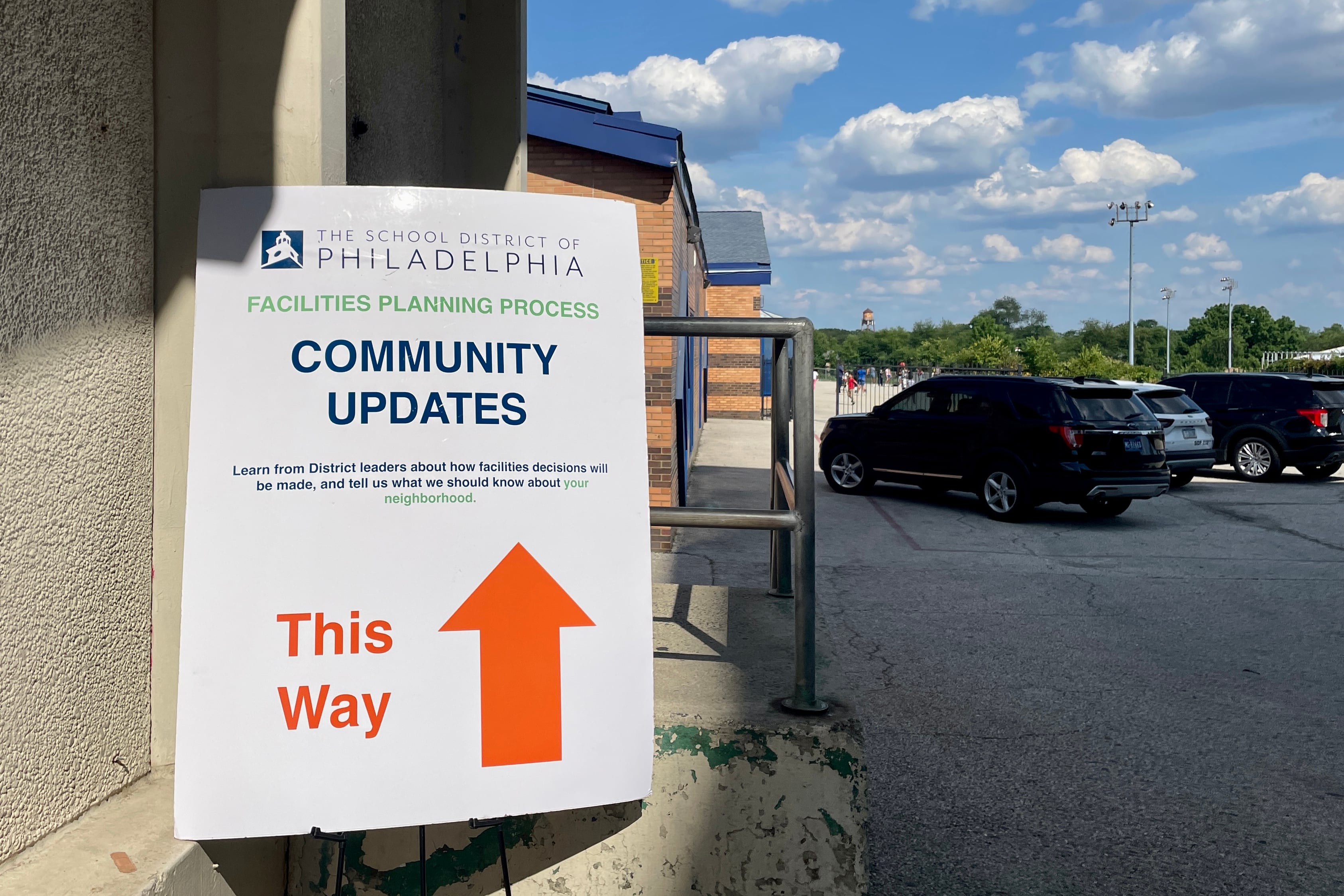 A photograph of a large sign outside near a building and a parking lot.