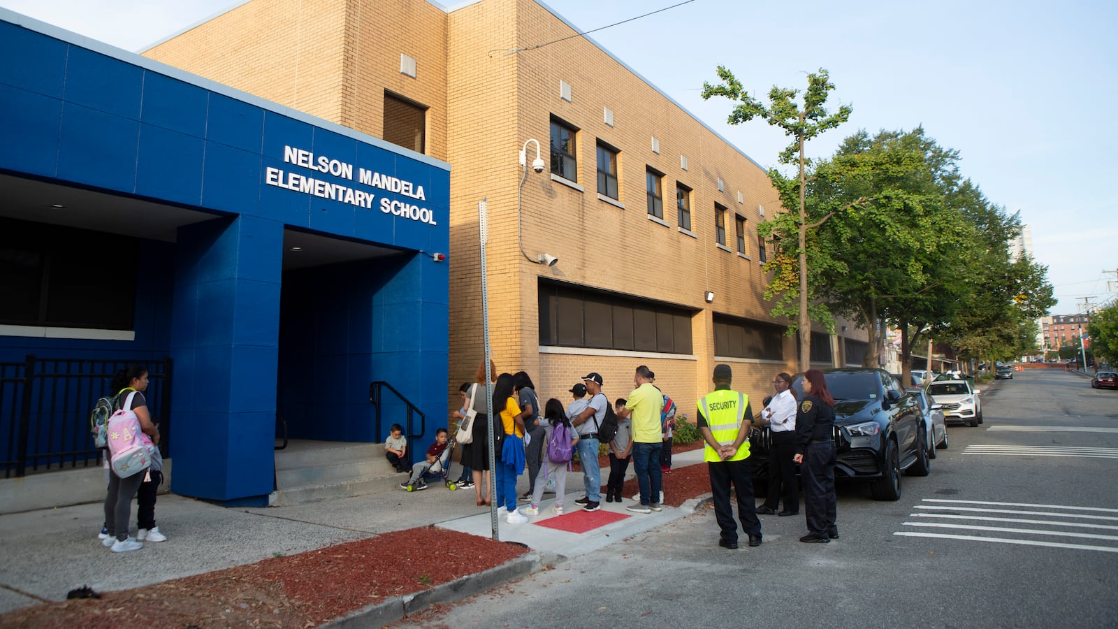 Students and parents make a line outside a concrete elementary school in Newark during the first day of school.