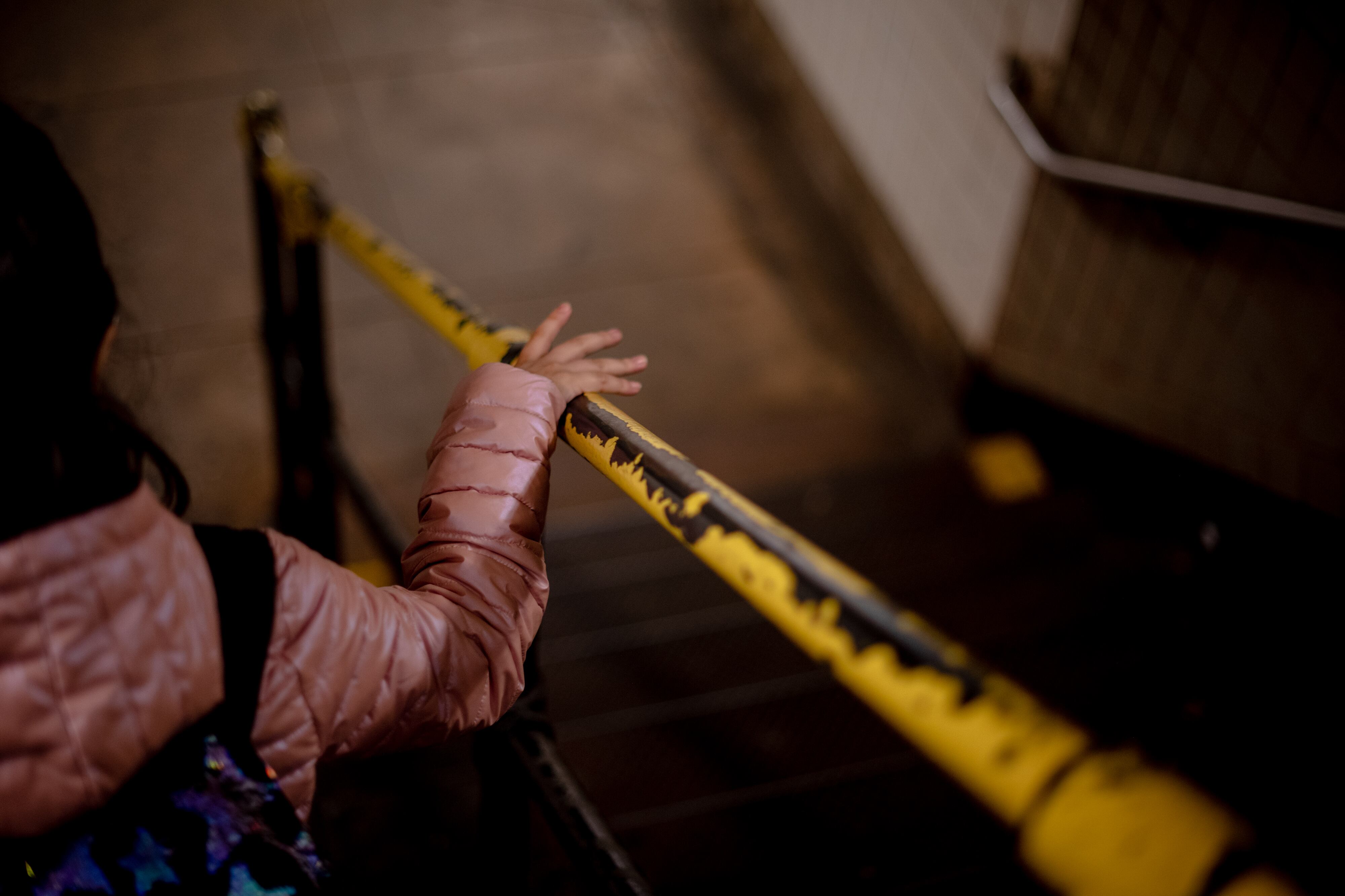 A close up of a young student's hand on a yellow and black railing in a stairwell going down to the train.