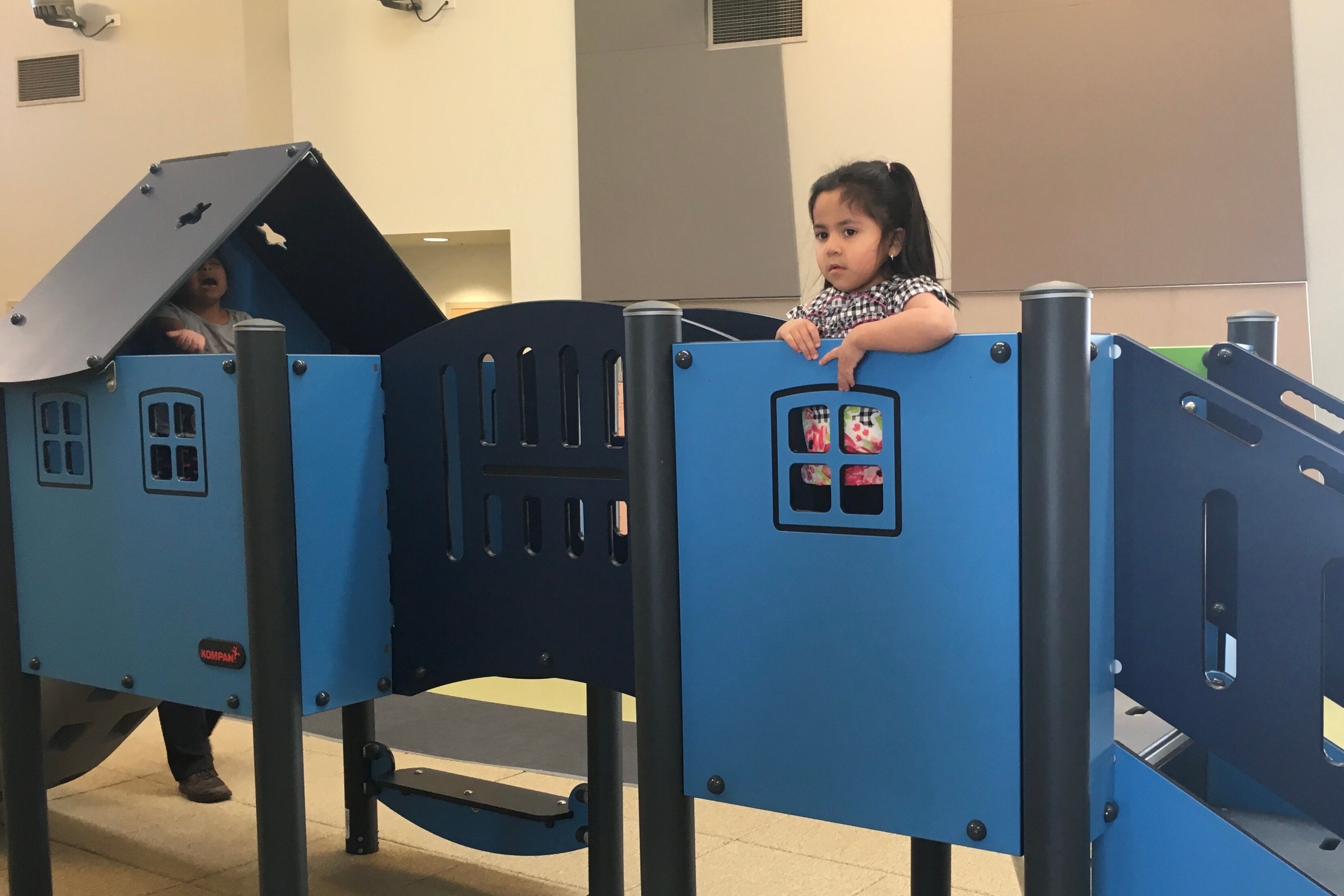 A preschool girl stand on top of a blue indoor play structure