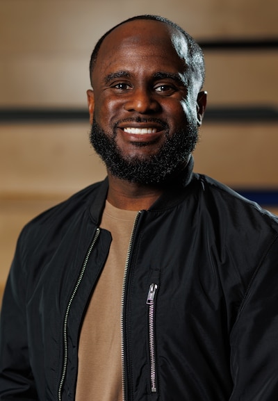 Headshot of a man with a beared wearing a tan shirt and a black jacket.