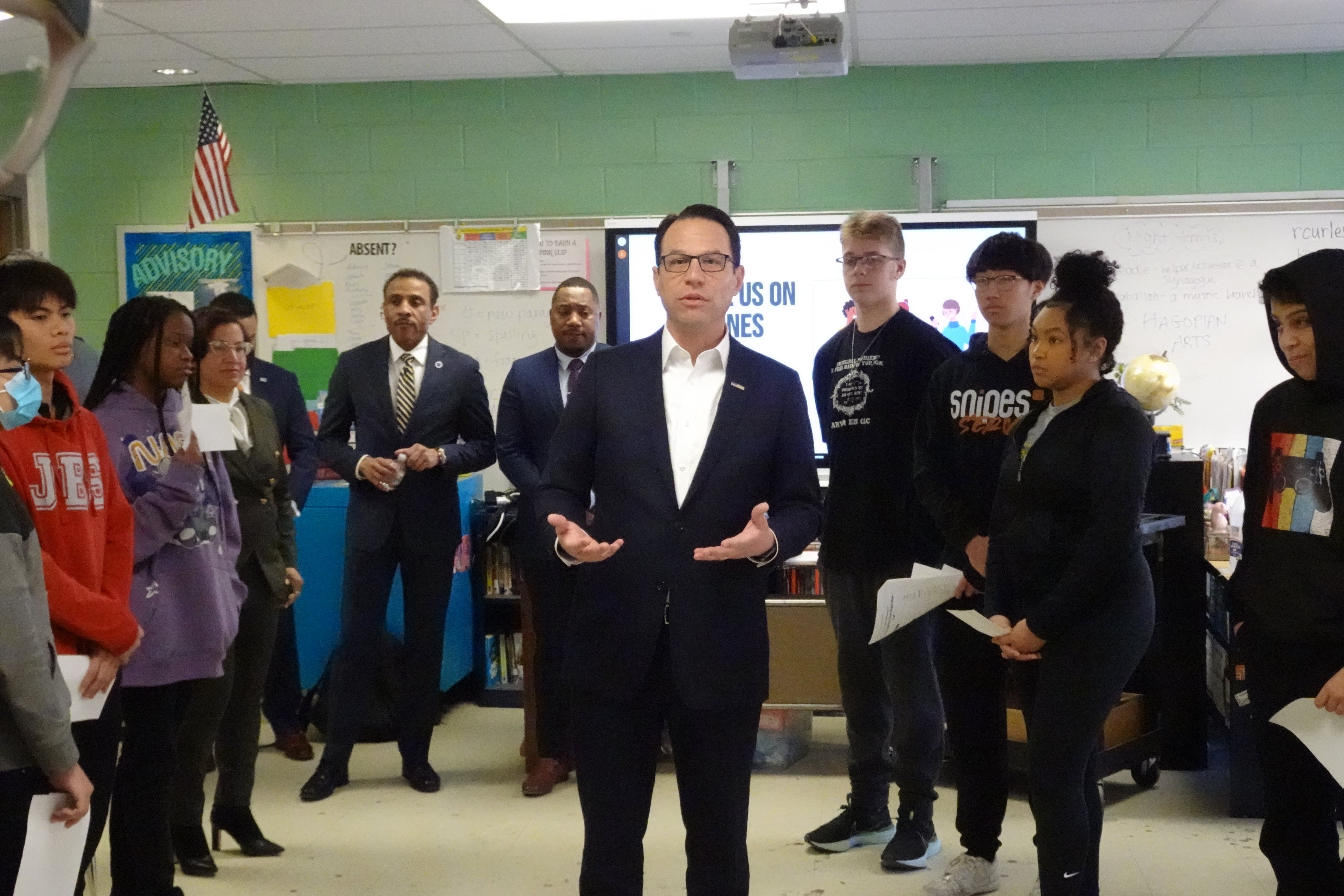 Governor Josh Shapiro, in a dark blue suit and white shirt, stands in a circle of students