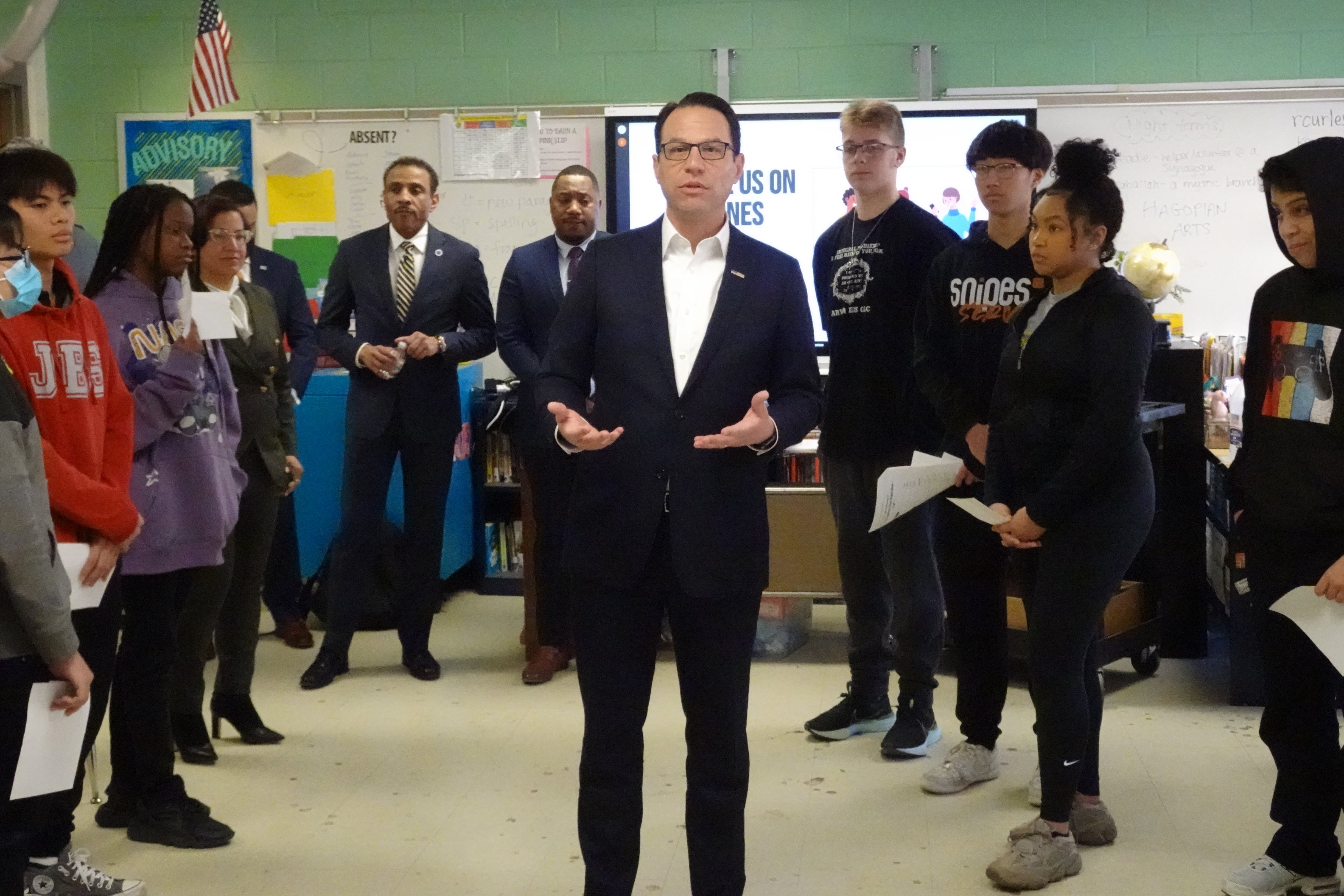 Governor Josh Shapiro, in a dark blue suit and white shirt, stands in a circle of students