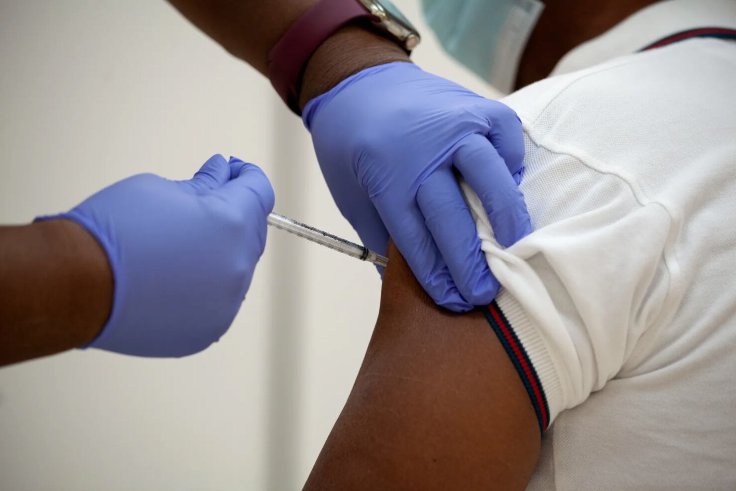 A health care worker wearing purple latex gloves gives a vaccine dose to a patient.