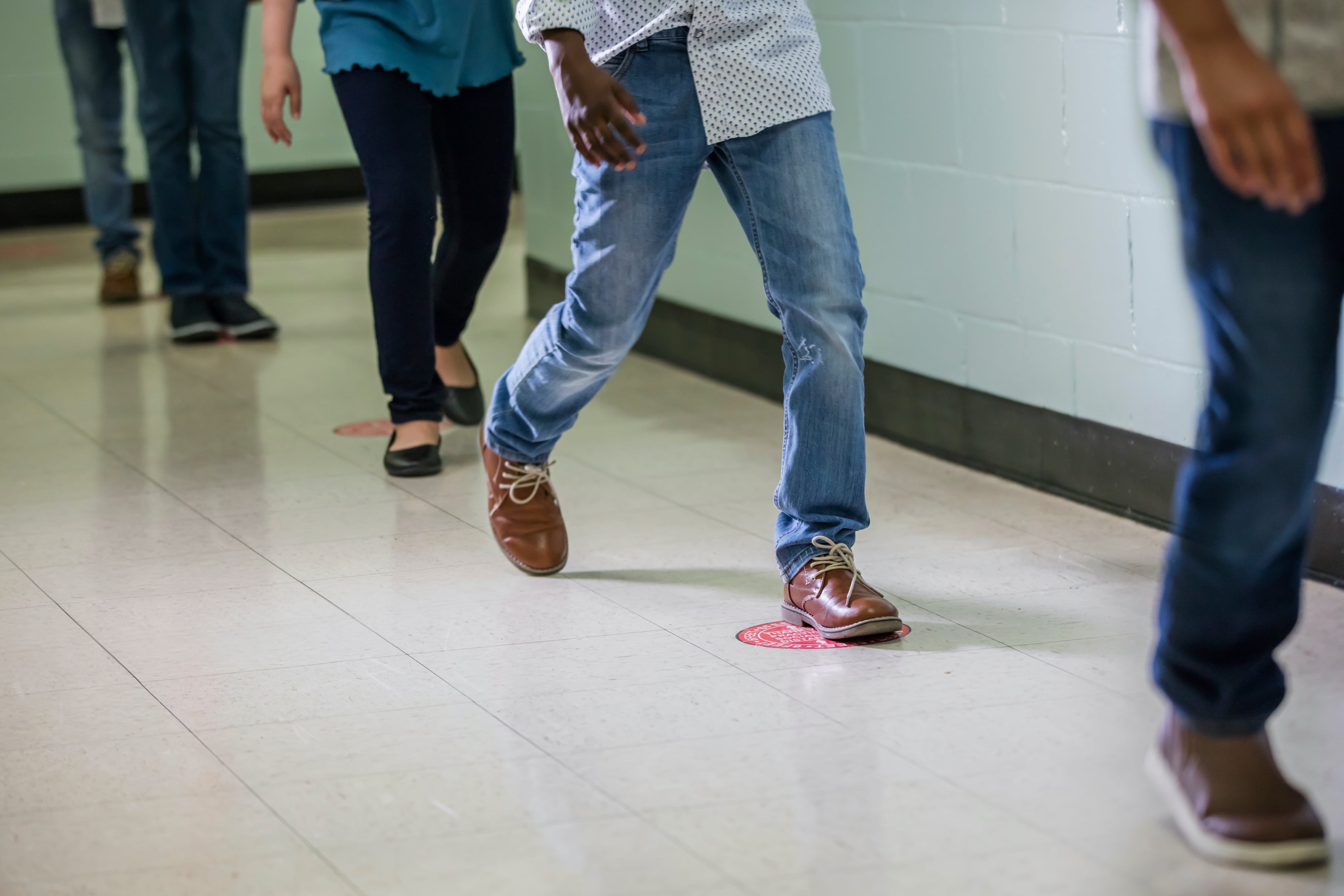 Cropped view of elementary students walking single file in a school hallway.