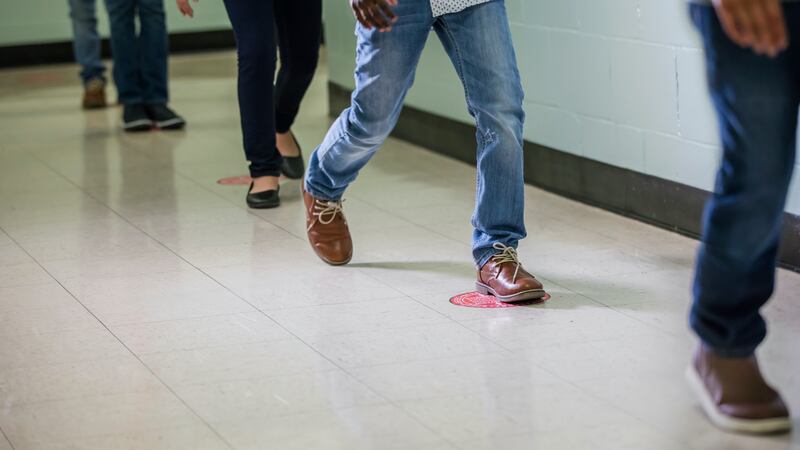 Cropped view of elementary students walking single file in a school hallway.