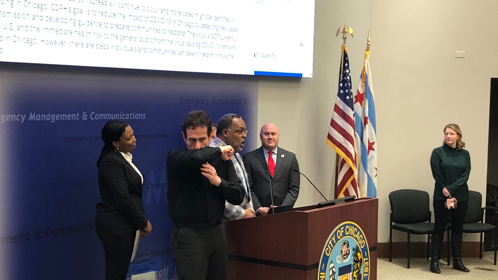 An interpreter demonstrates a proper coughing technique at a Tuesday press conference attended by Chicago schools chief Janice Jackson, left, the district’s Chief Health Officer Kenneth Fox, speaking, and Jennifer Layden, far right, deputy commissioner for the city’s health department.