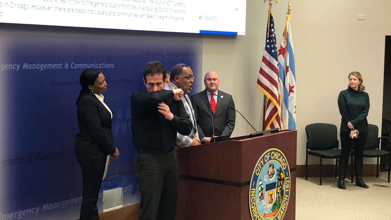 An interpreter demonstrates a proper coughing technique at a Tuesday press conference attended by Chicago schools chief Janice Jackson, left, the district’s Chief Health Officer Kenneth Fox, speaking, and Jennifer Layden, far right, deputy commissioner for the city’s health department.