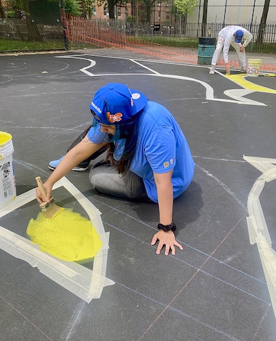 A student in blue paints on a playground surface.