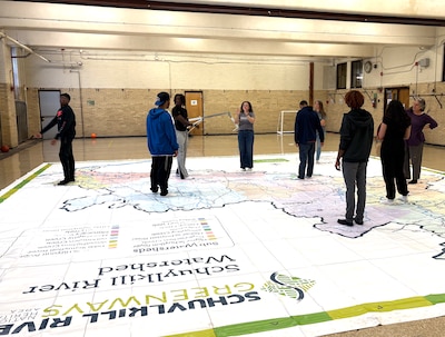 A photograph of a group of high school students in a large room with a giant map on the floor.